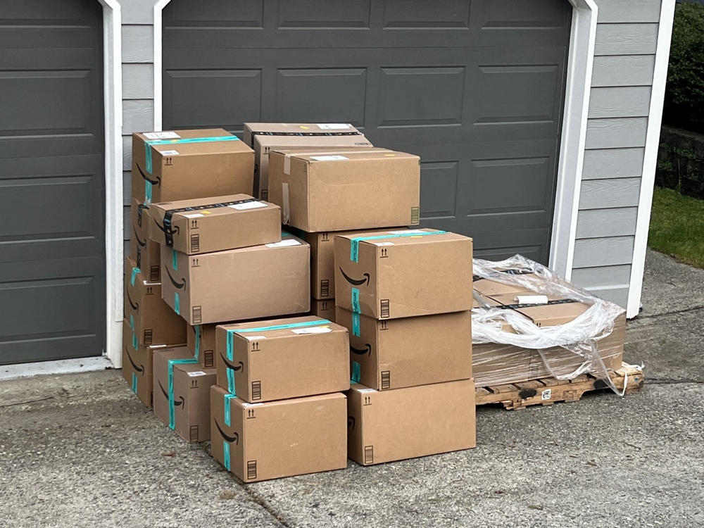 A large stack of empty Amazon cardboard shipping boxes on a pallet waiting for pickup in front of a Bellingham garage.