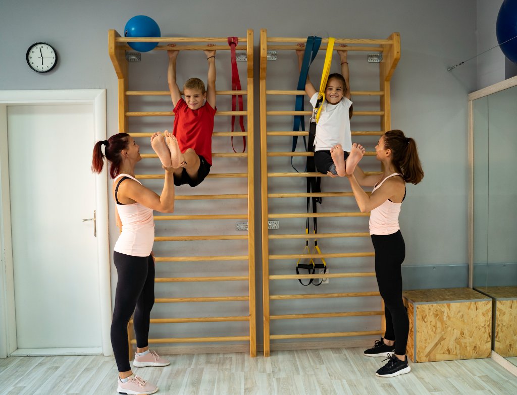 Zwei Kinder turnen an Sprossenwand mit zwei Trainerinnen