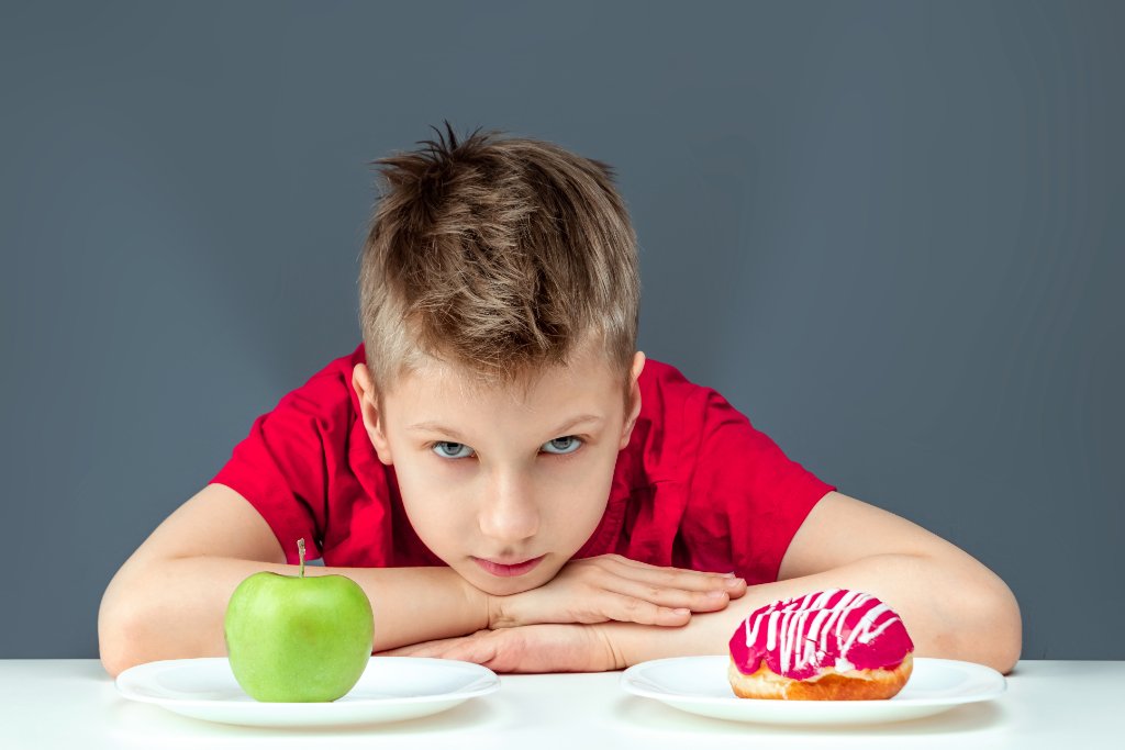 Kind schaut nachdenklich auf Donut und Apfel