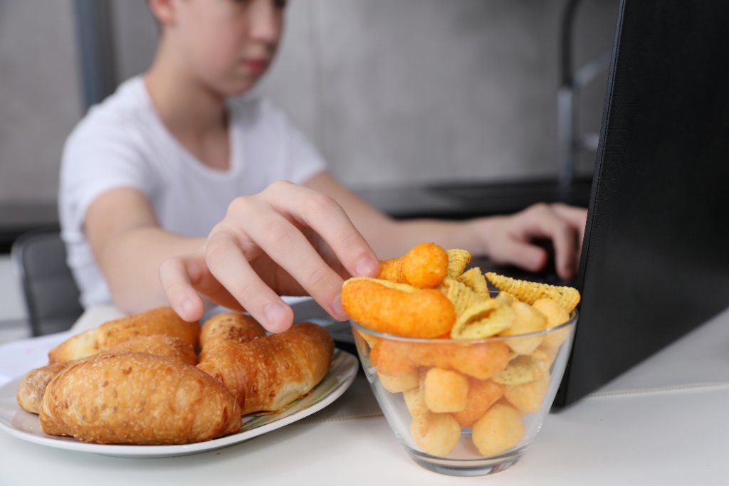 Kind greift nach Snacks vor dem Laptop