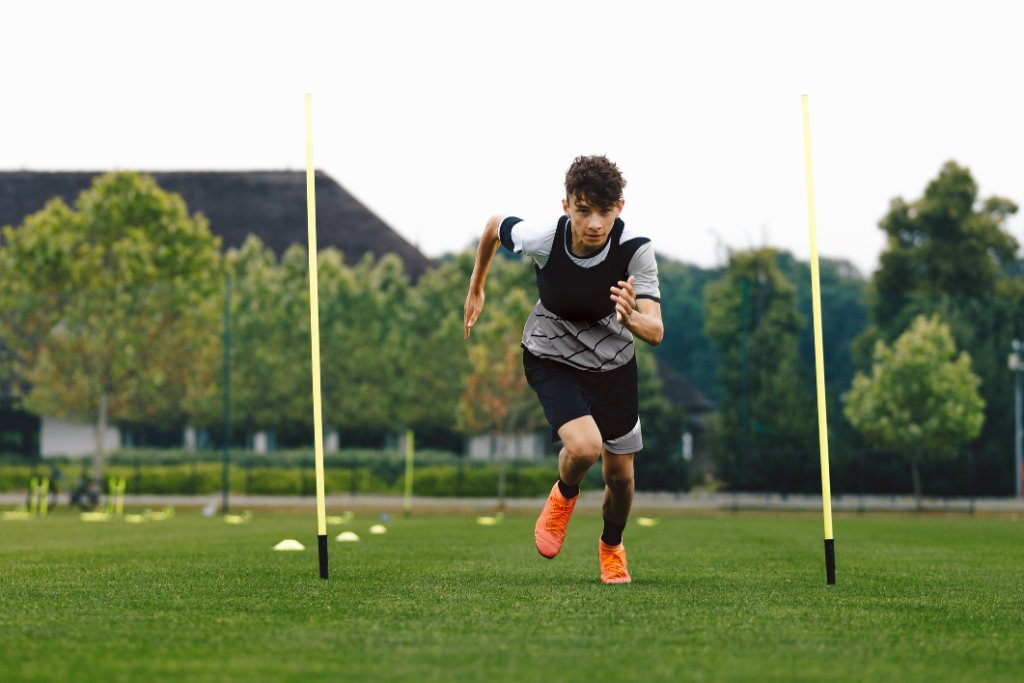 Jugendlicher sprintet auf Sportplatz zwischen Stangen