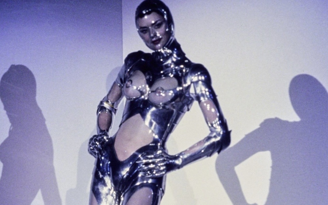Thierry Mugler's chrome metallic robot bodysuit from the Autumn/Winter 1995 haute couture collection, with a high collar and sculptural cut-outs, casting sharp shadows on the studio wall.