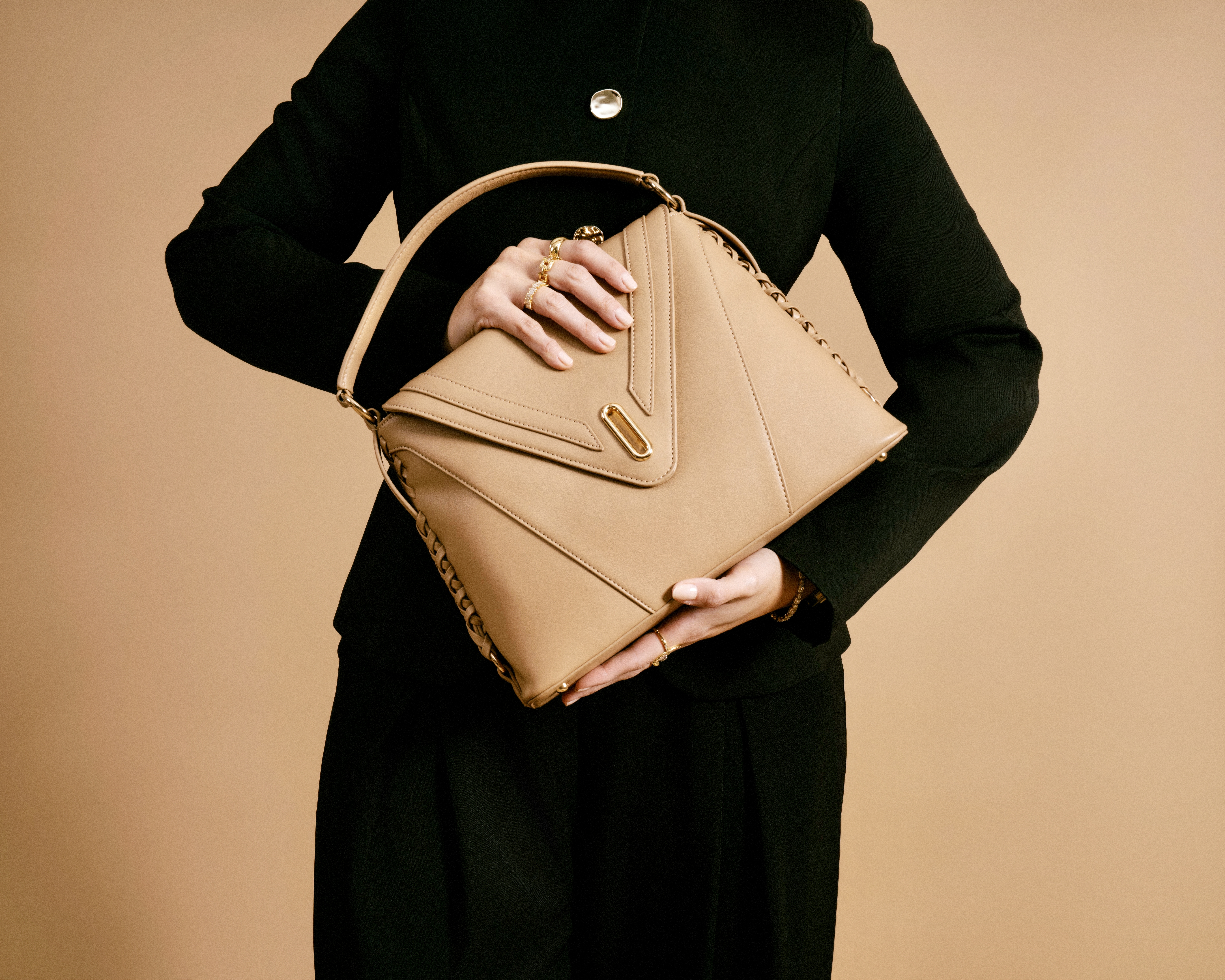 Close-up of THE VESSEL against black tailoring, emphasizing the natural leather, stitching, central gold-tone hardware, and side lacing.