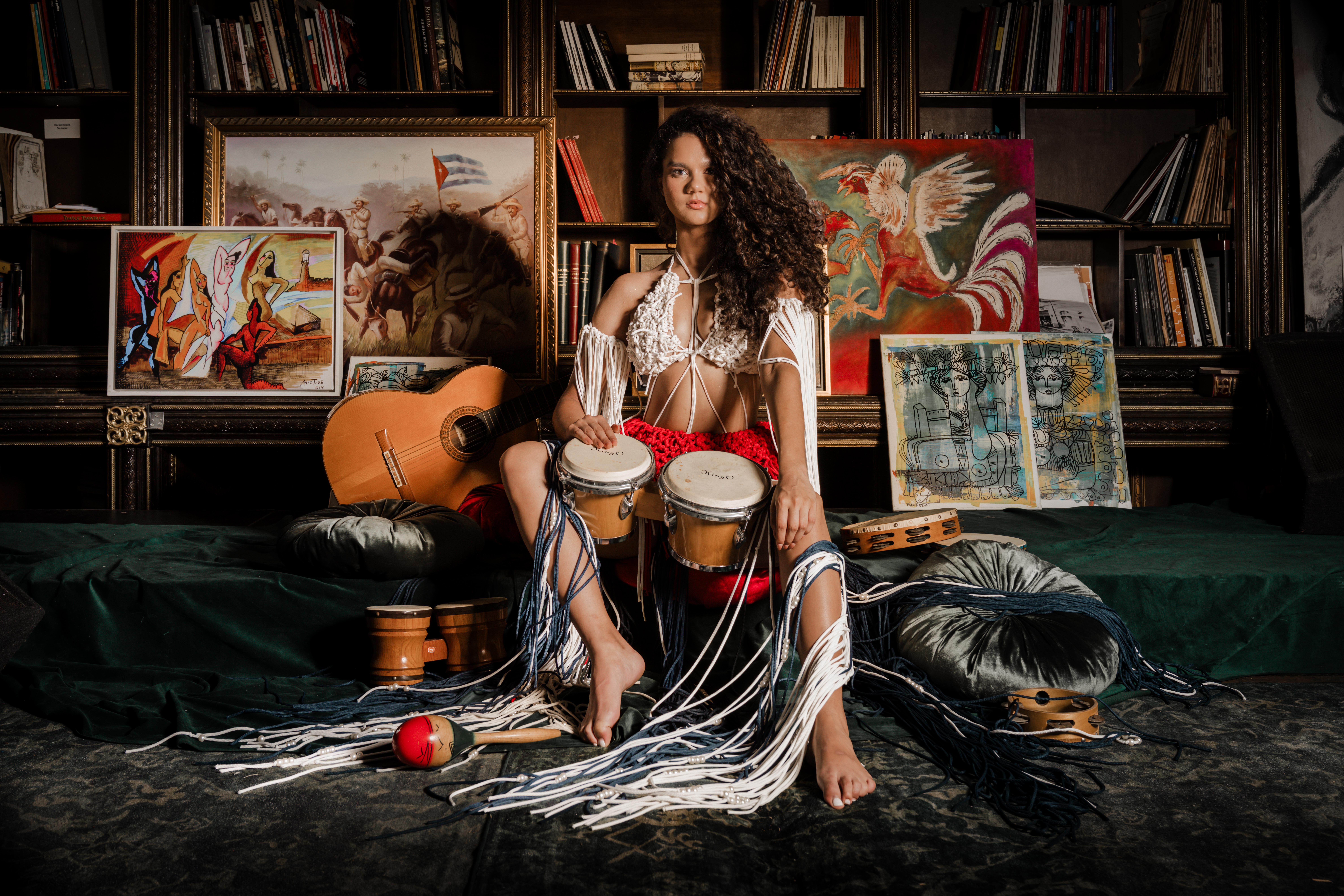 The model seated among percussion instruments, wearing the ISALOR Untitled Textile Composition