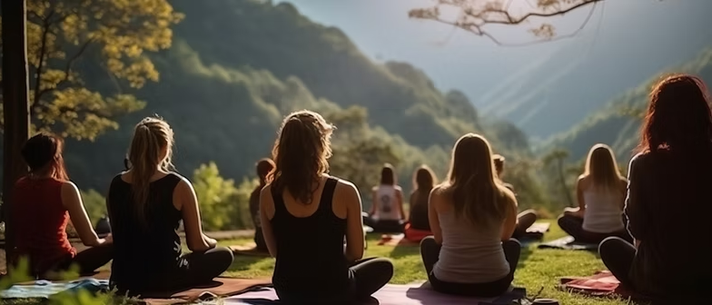 Group practicing yoga on a grassy hilltop overlooking mountains