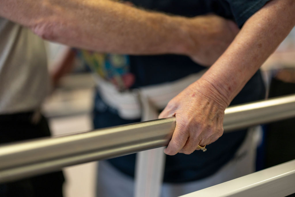 A caregiver's hand supporting a resident's hand on a grab bar