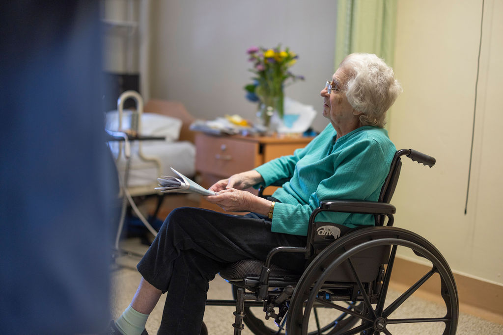 A resident reading in her room — comfort and familiarity.
