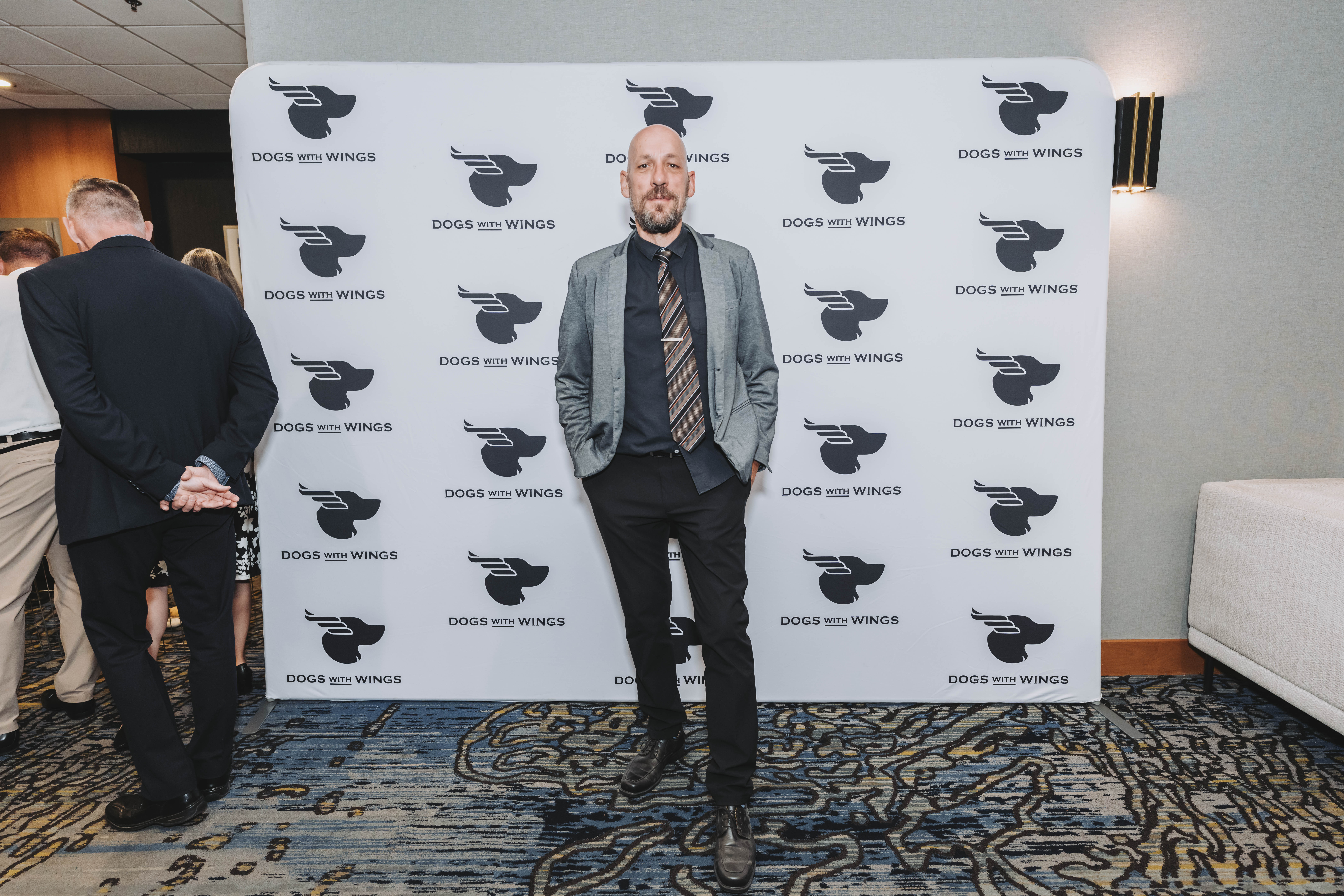 A guest in a grey blazer standing at the gala backdrop