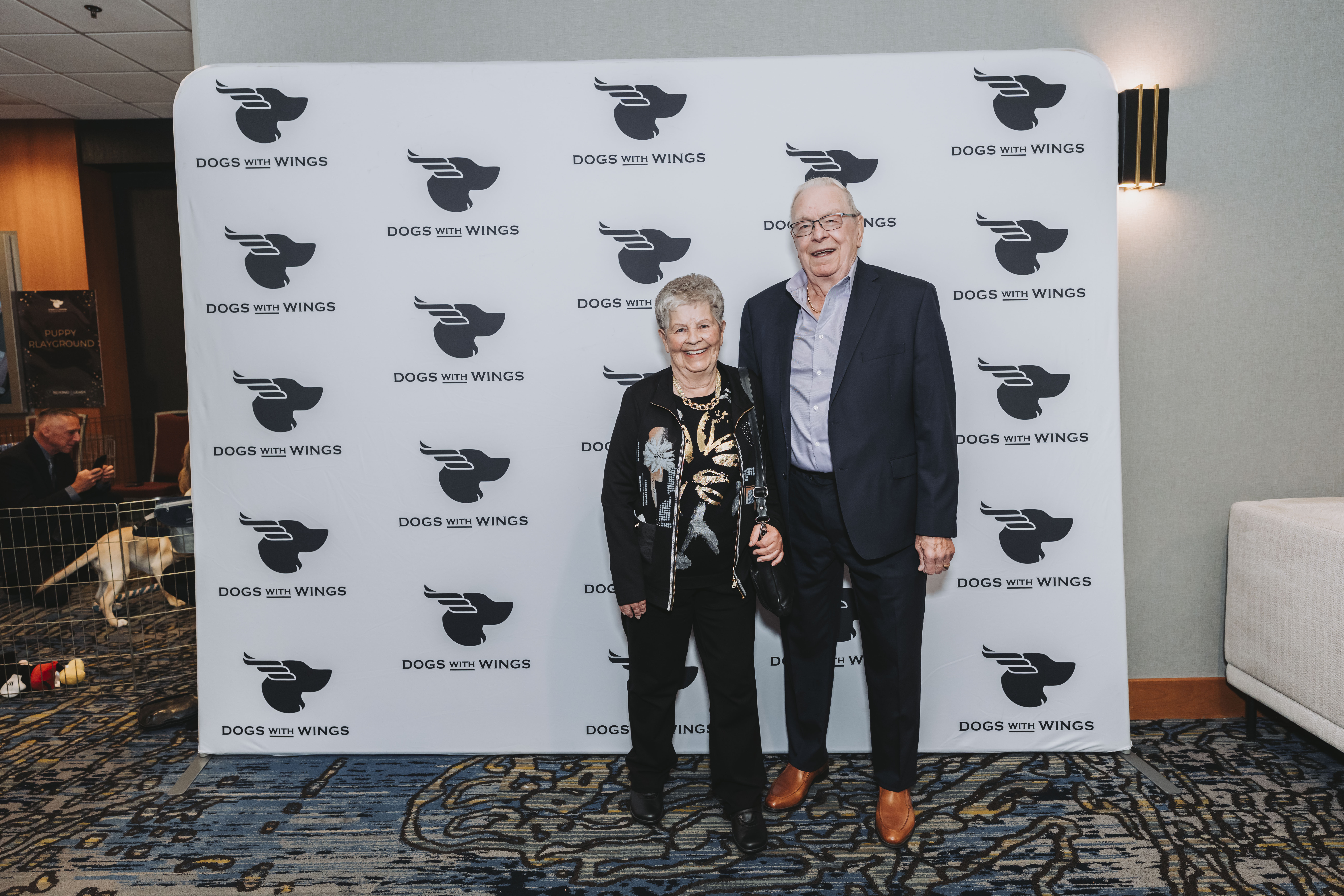 A couple smiling together at the Dogs With Wings backdrop