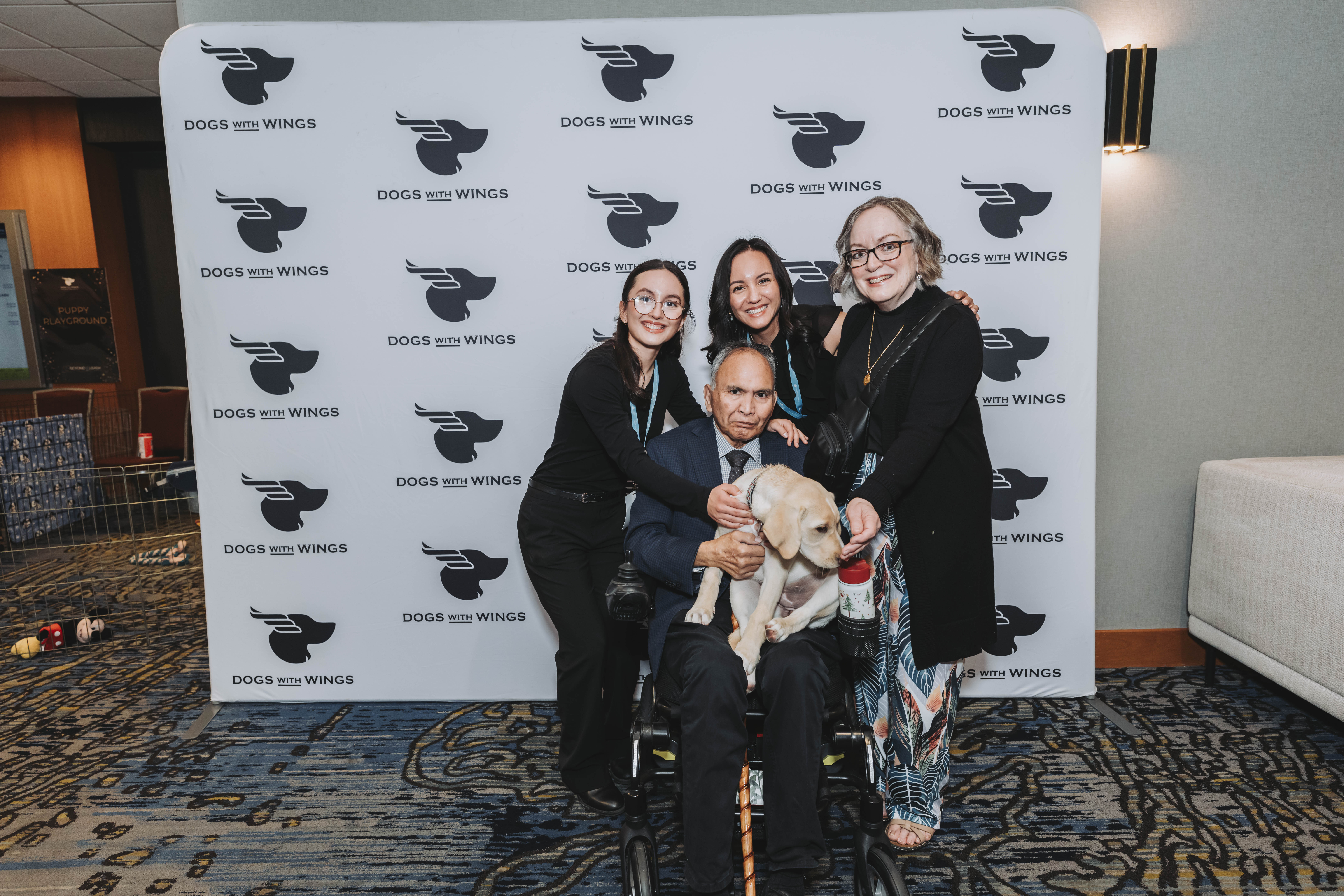 Guests posing with a yellow Labrador puppy at the gala backdrop