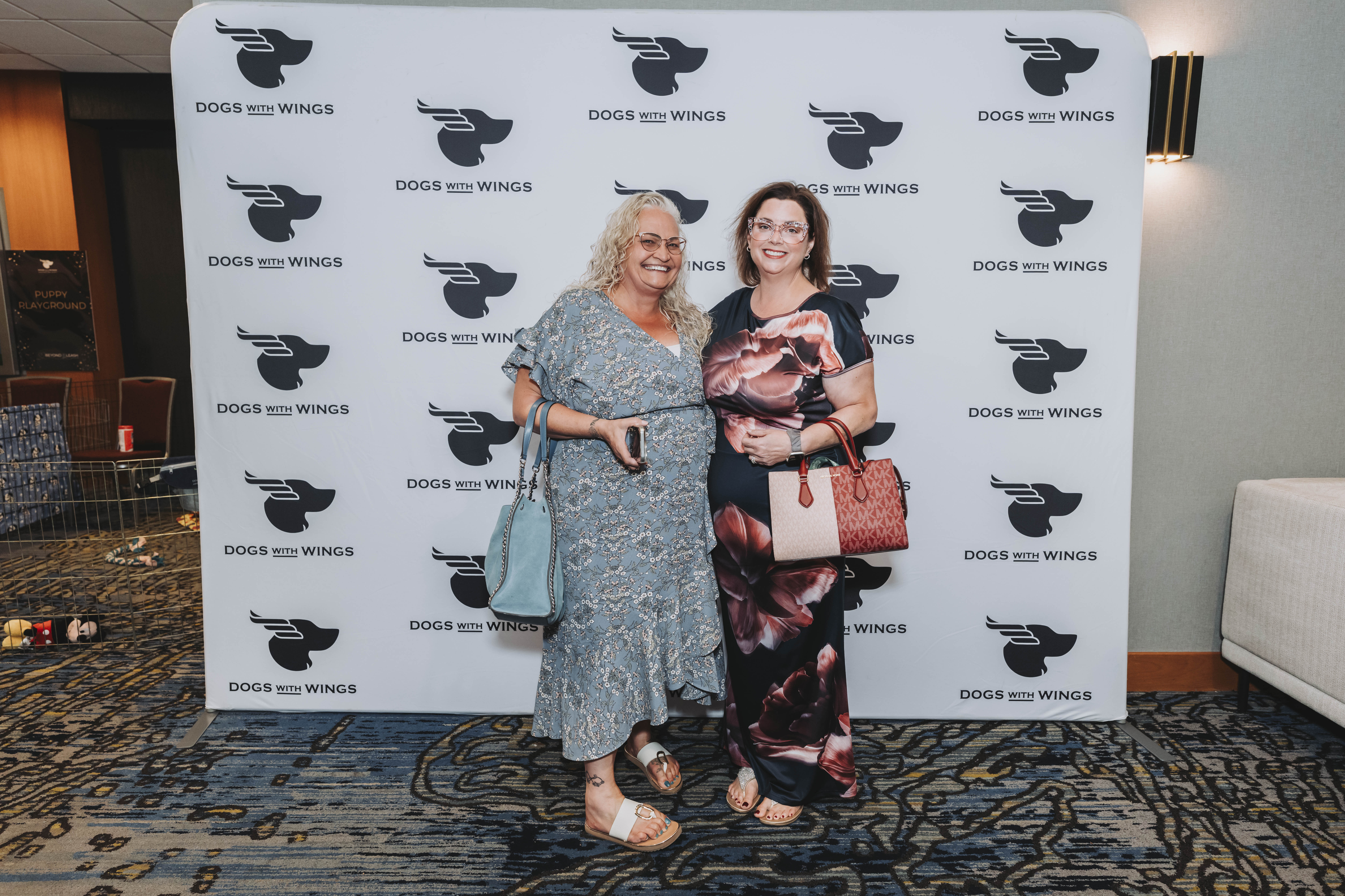 Two guests in floral dresses posing at the gala photo wall