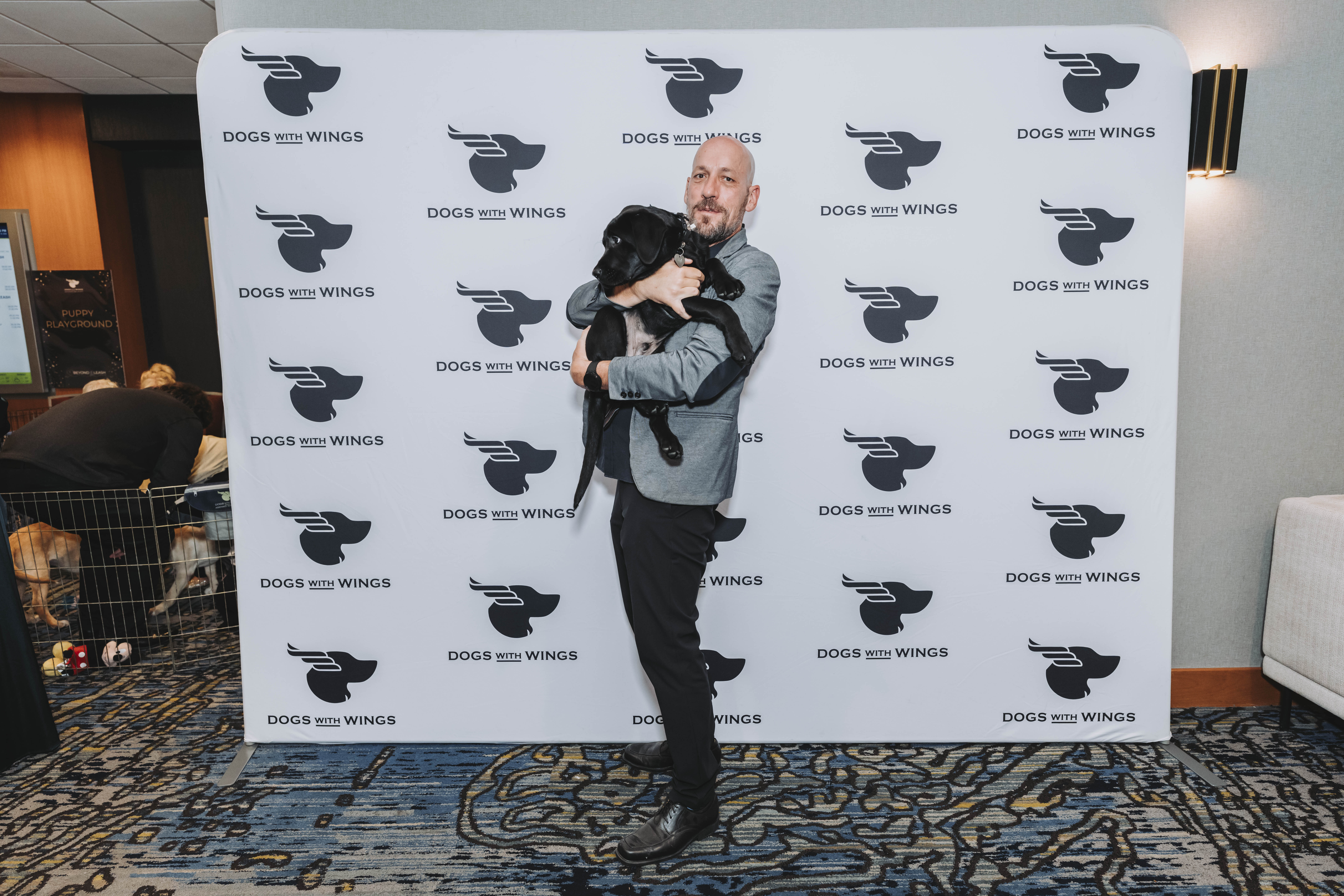 A guest holding a black puppy at the photo wall