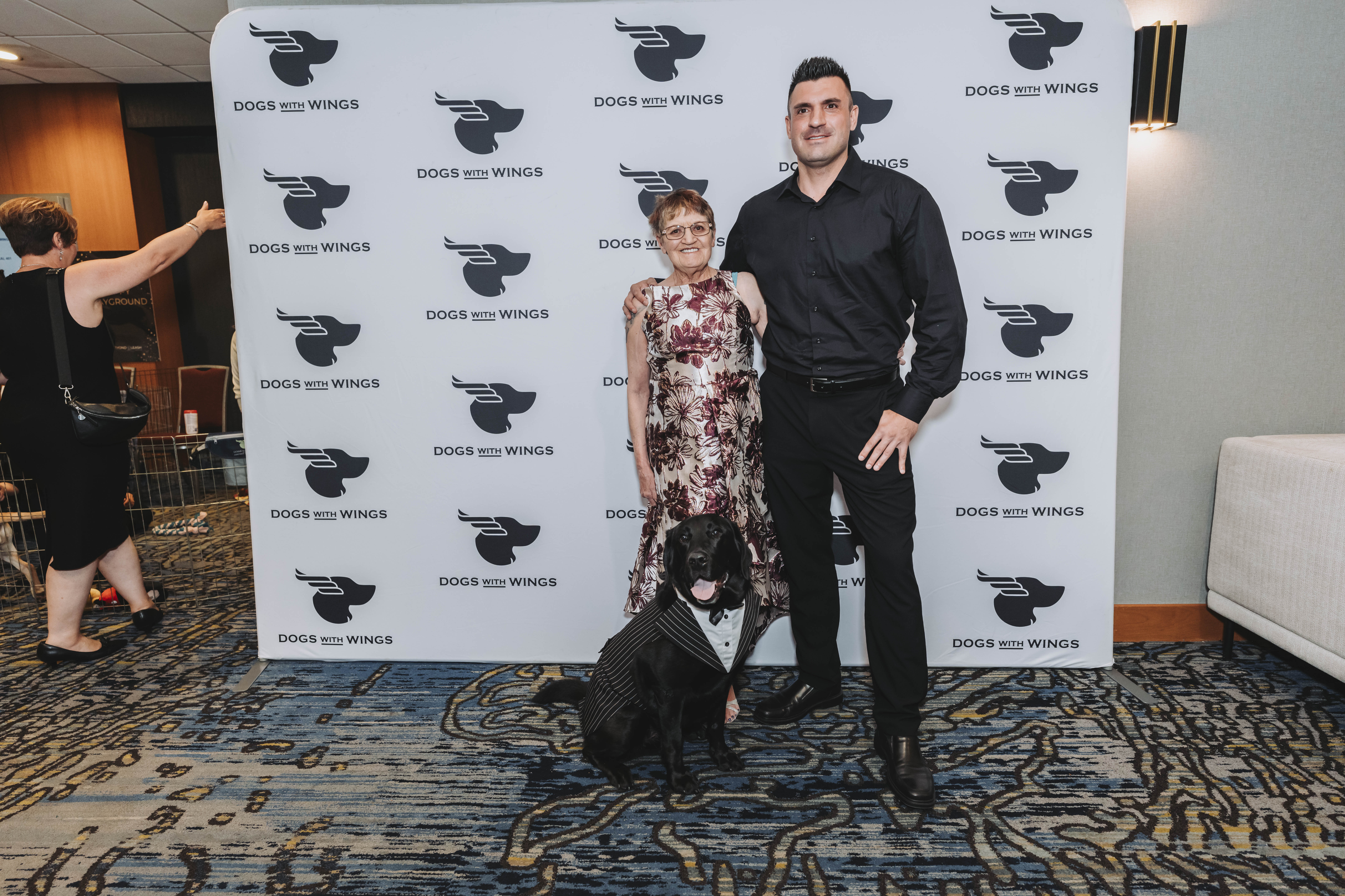 A couple posing with a black dog in a pinstripe tuxedo vest