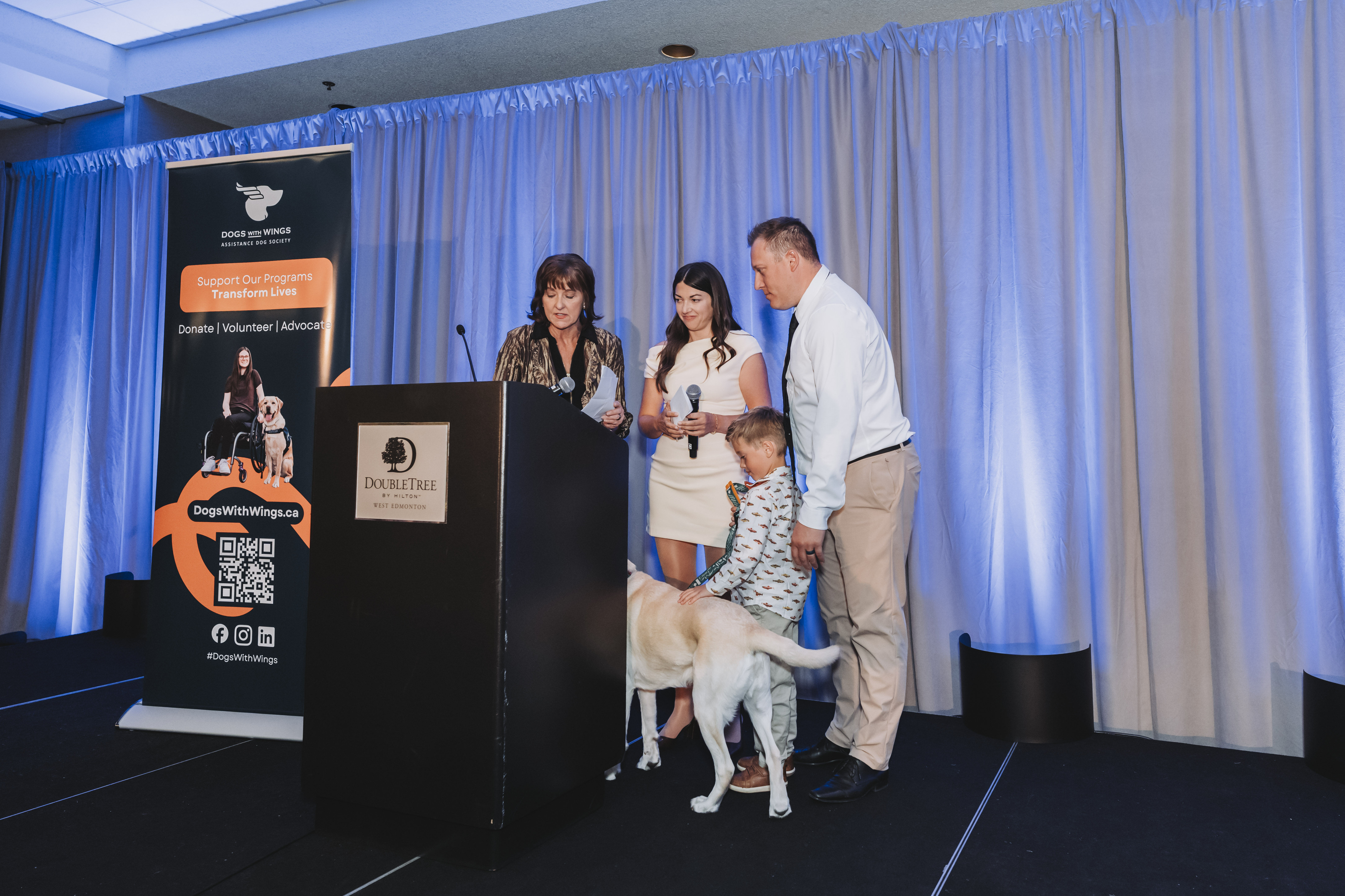 Guests on stage with a young guest meeting a yellow Labrador service dog