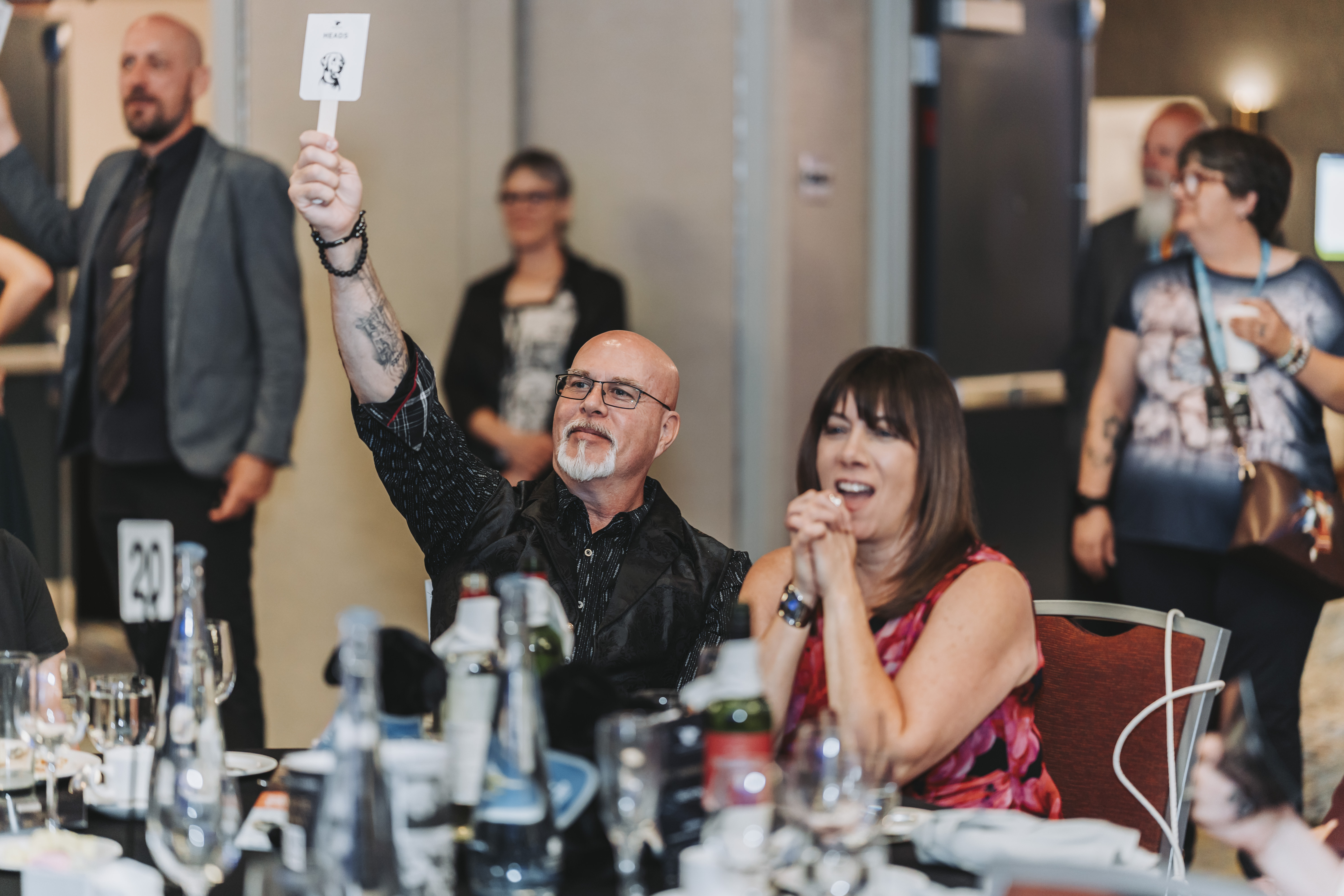 A guest raising a Heads paddle beside an excited tablemate
