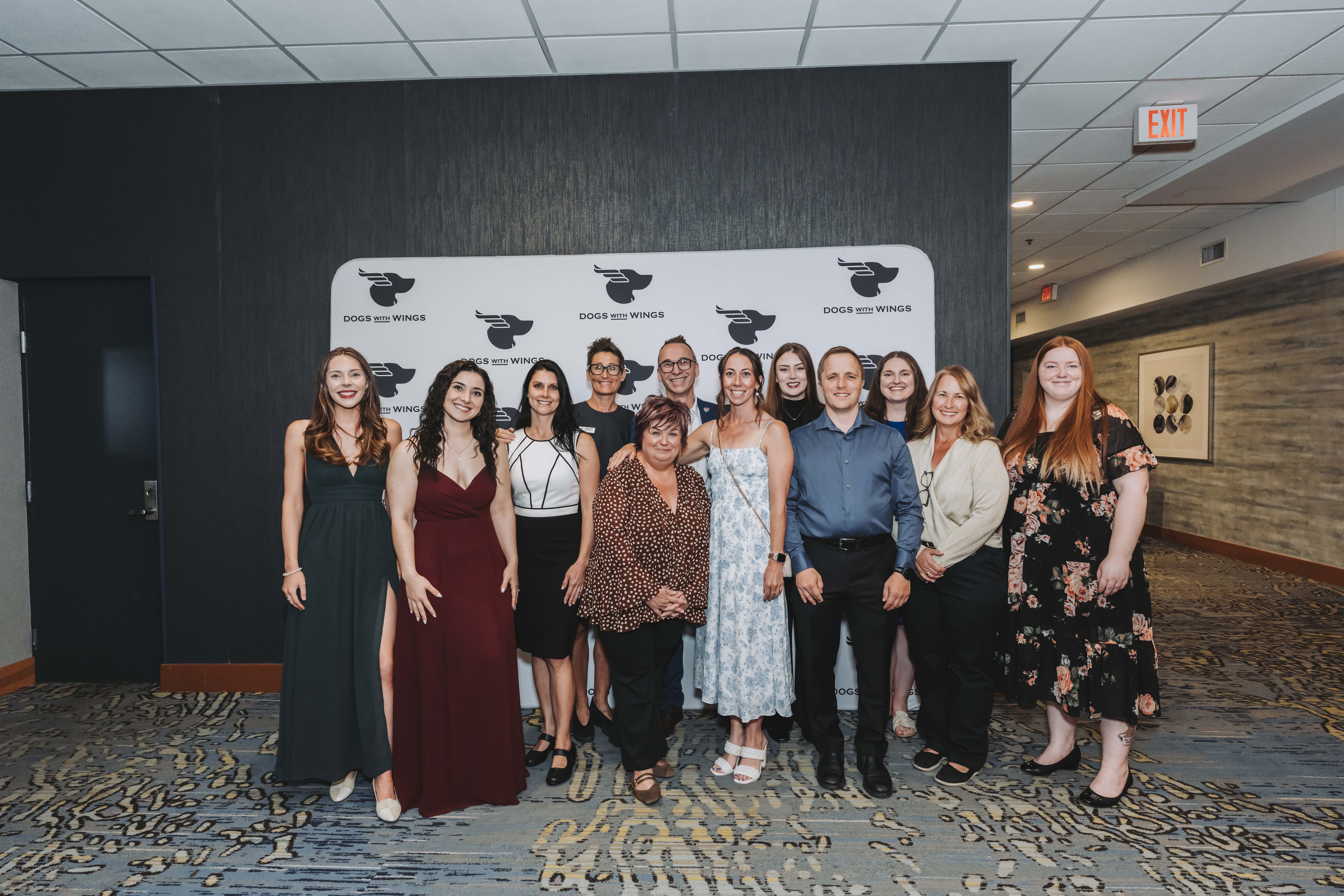 A group of guests posing in front of the Dogs With Wings backdrop