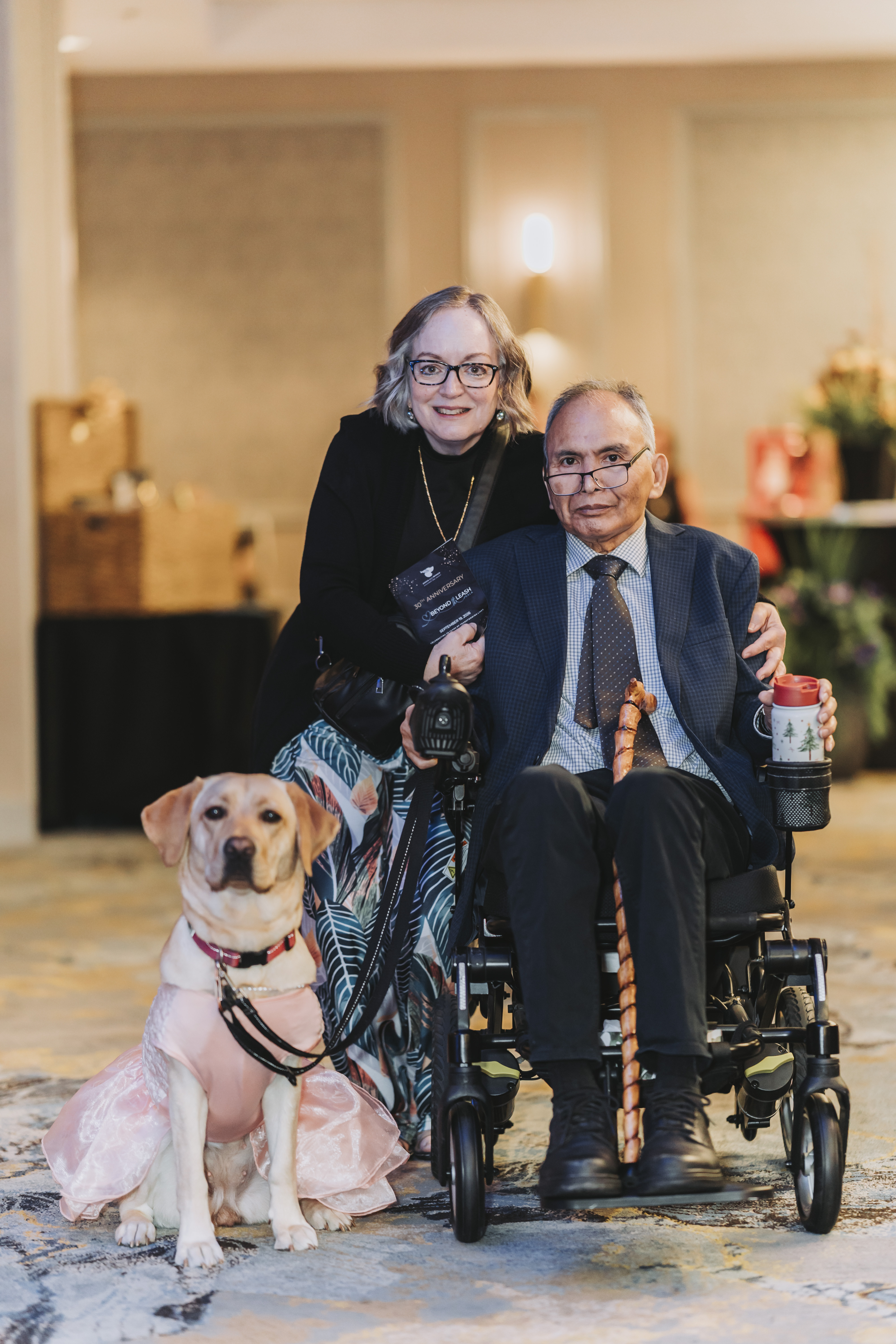 Guests posing with a yellow Labrador in a pink dress at the gala