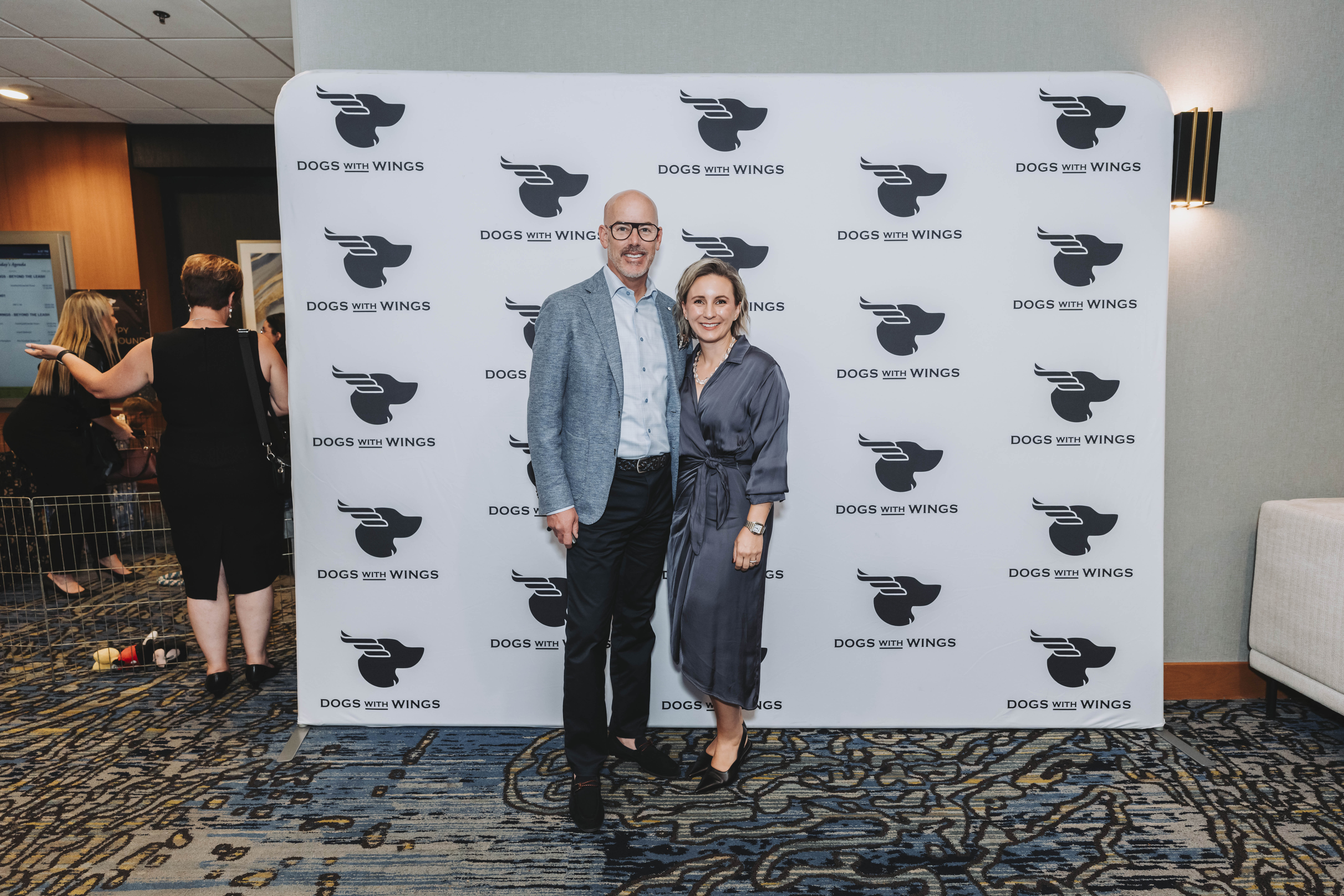 A couple smiling at the Dogs With Wings backdrop