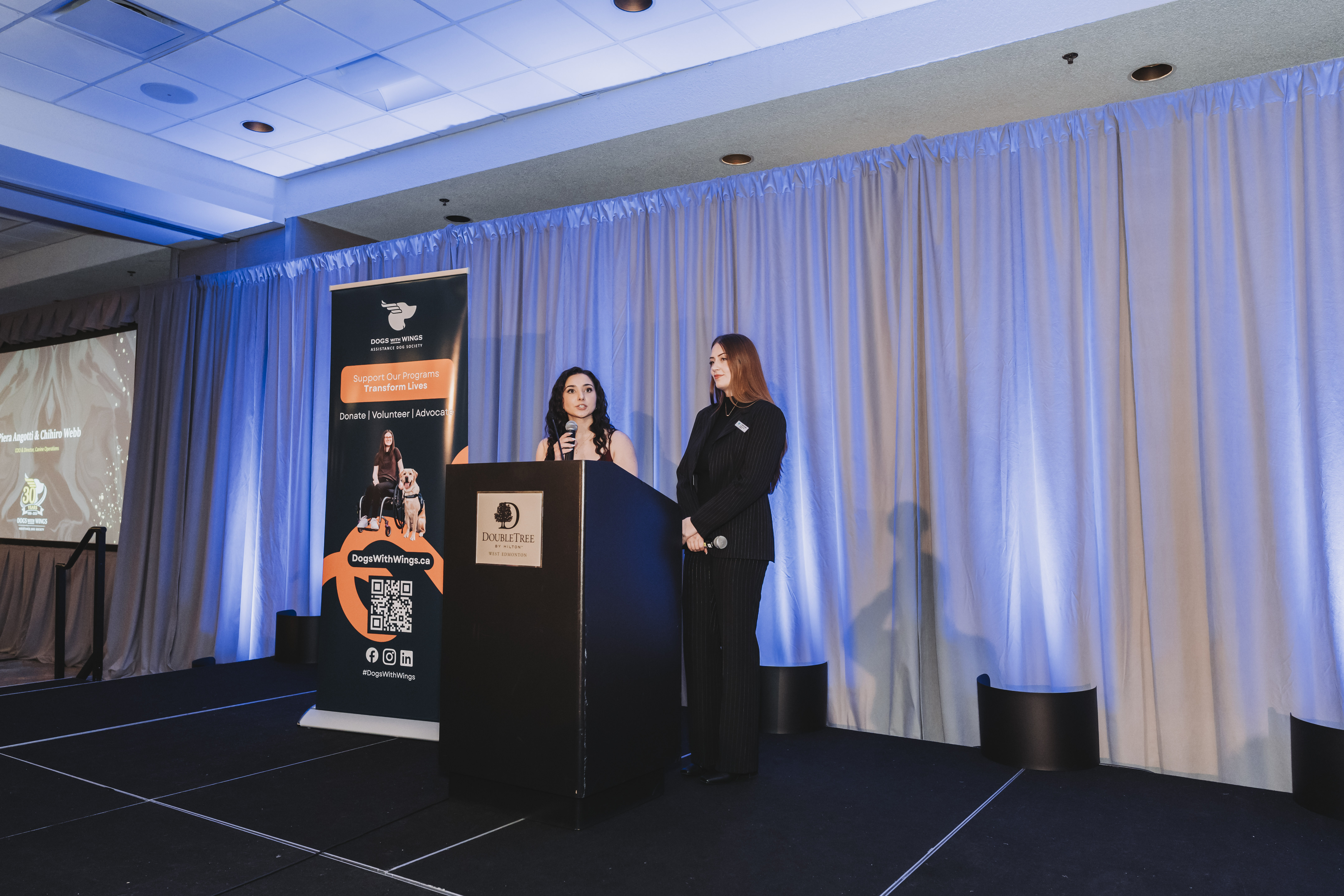 Two presenters on stage beside the gala banner and podium
