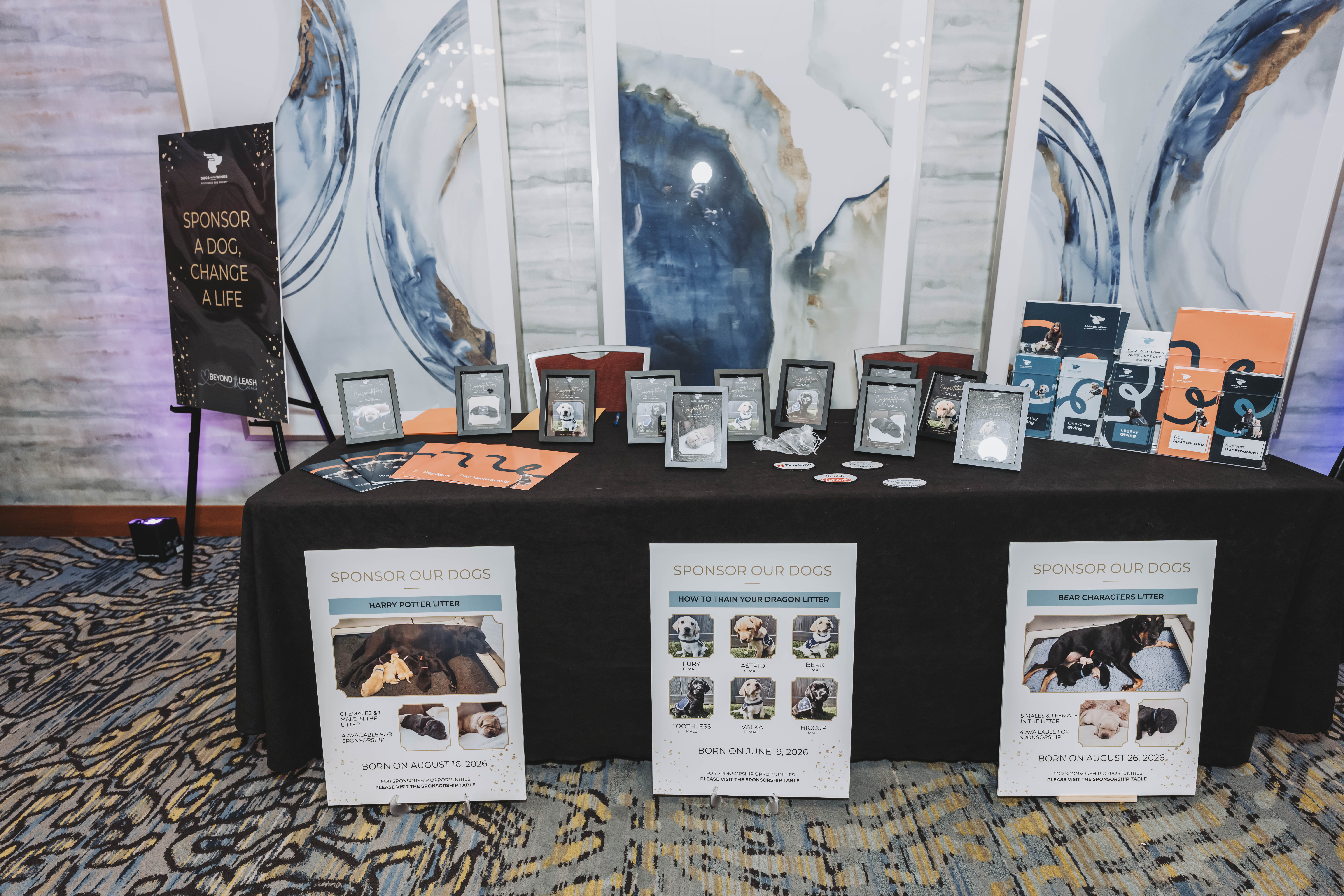 The Sponsor Our Dogs table with litter posters and framed portraits