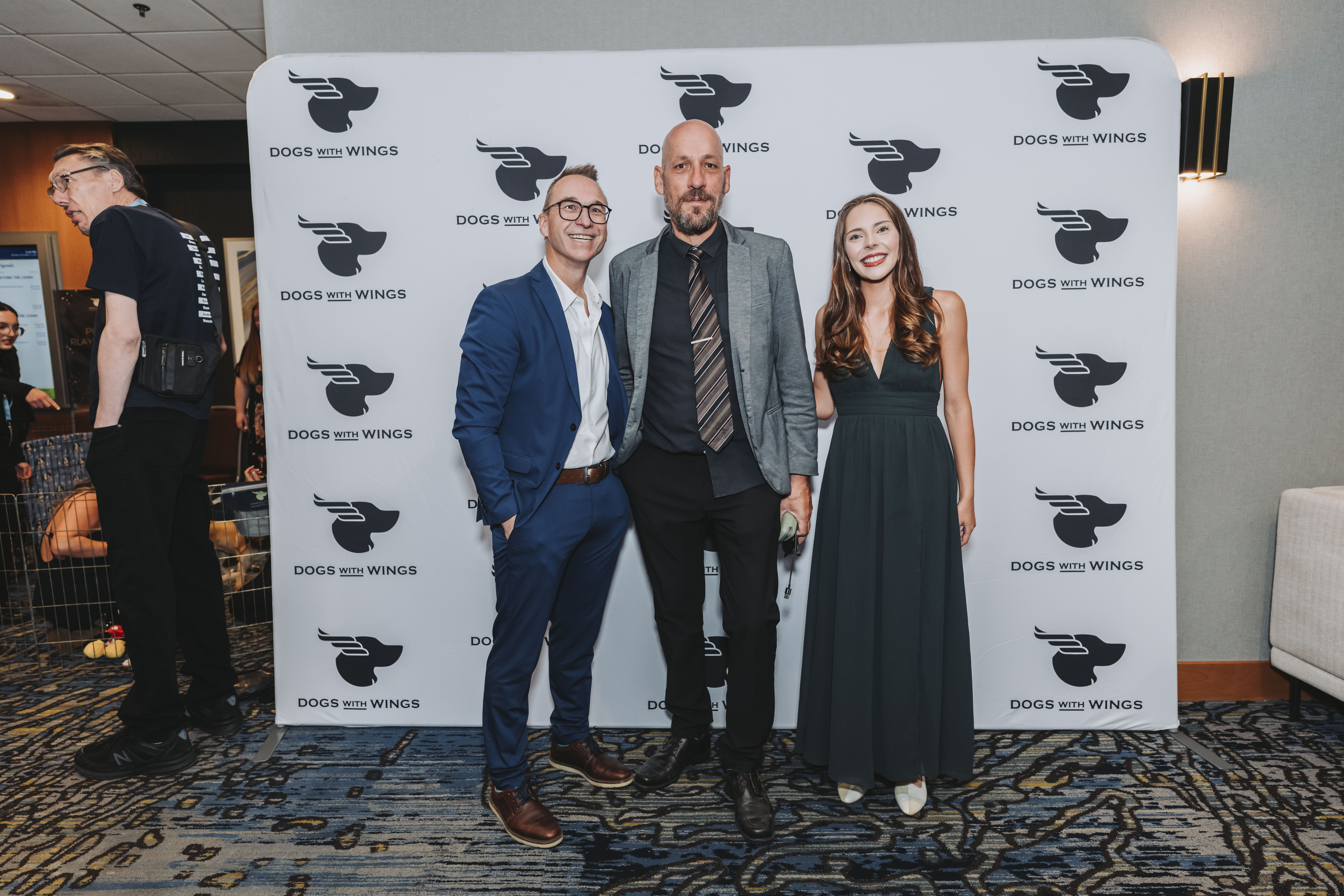 Three guests together in front of the Dogs With Wings backdrop