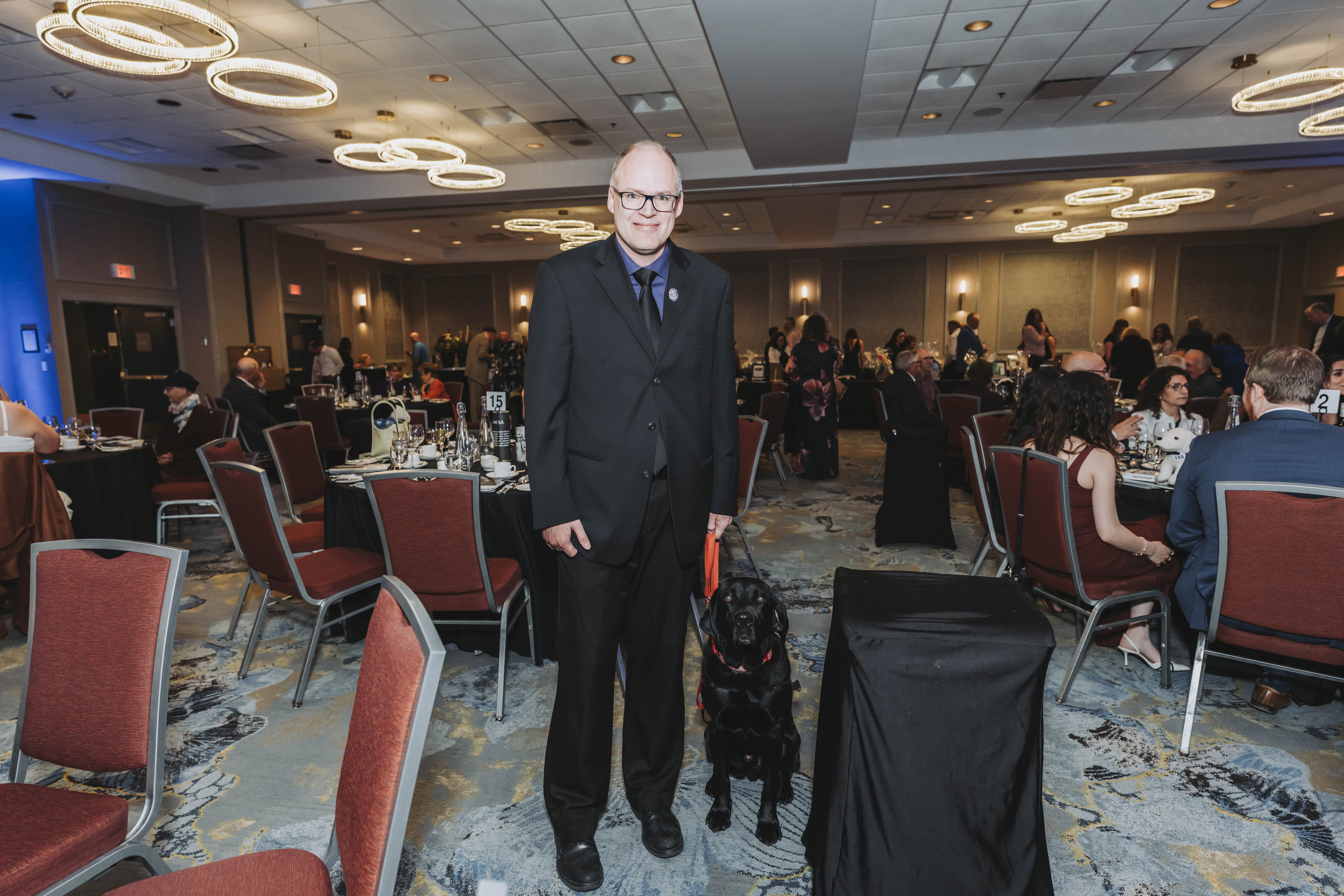 A guest standing with a black assistance dog in the ballroom