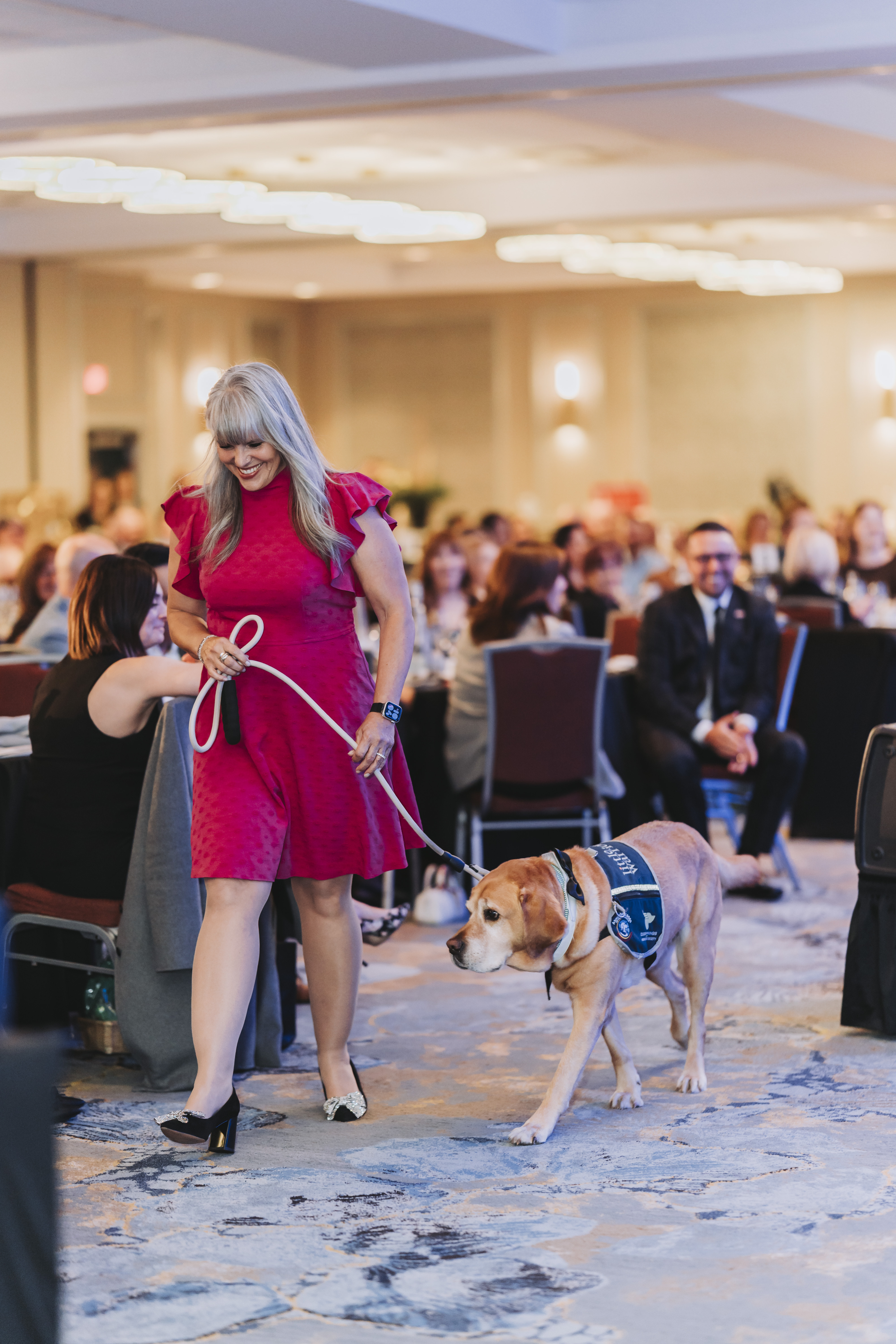 A guest walking a Little Wings service dog through the ballroom