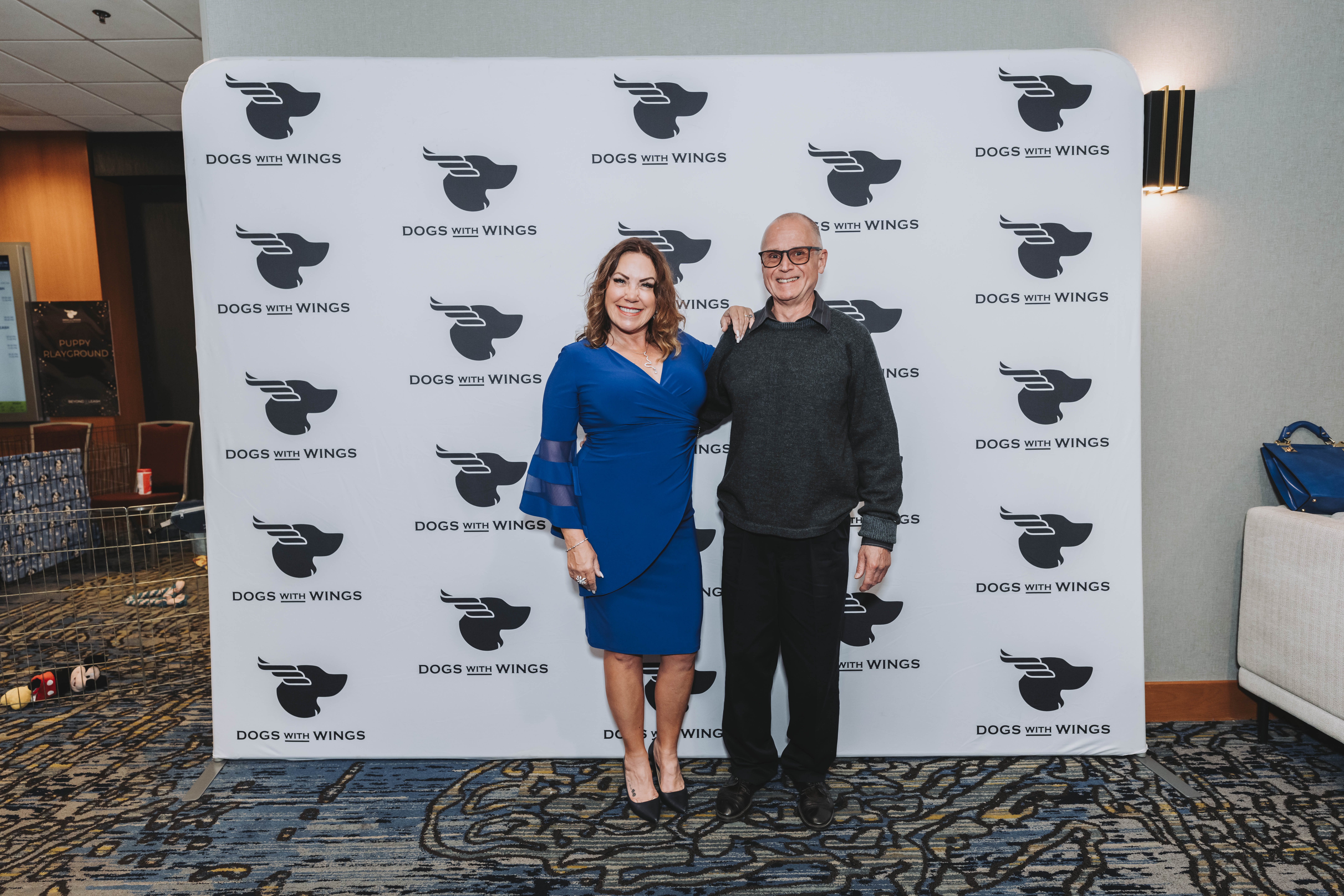 A couple posing at the gala photo wall, with the puppy playground beside them