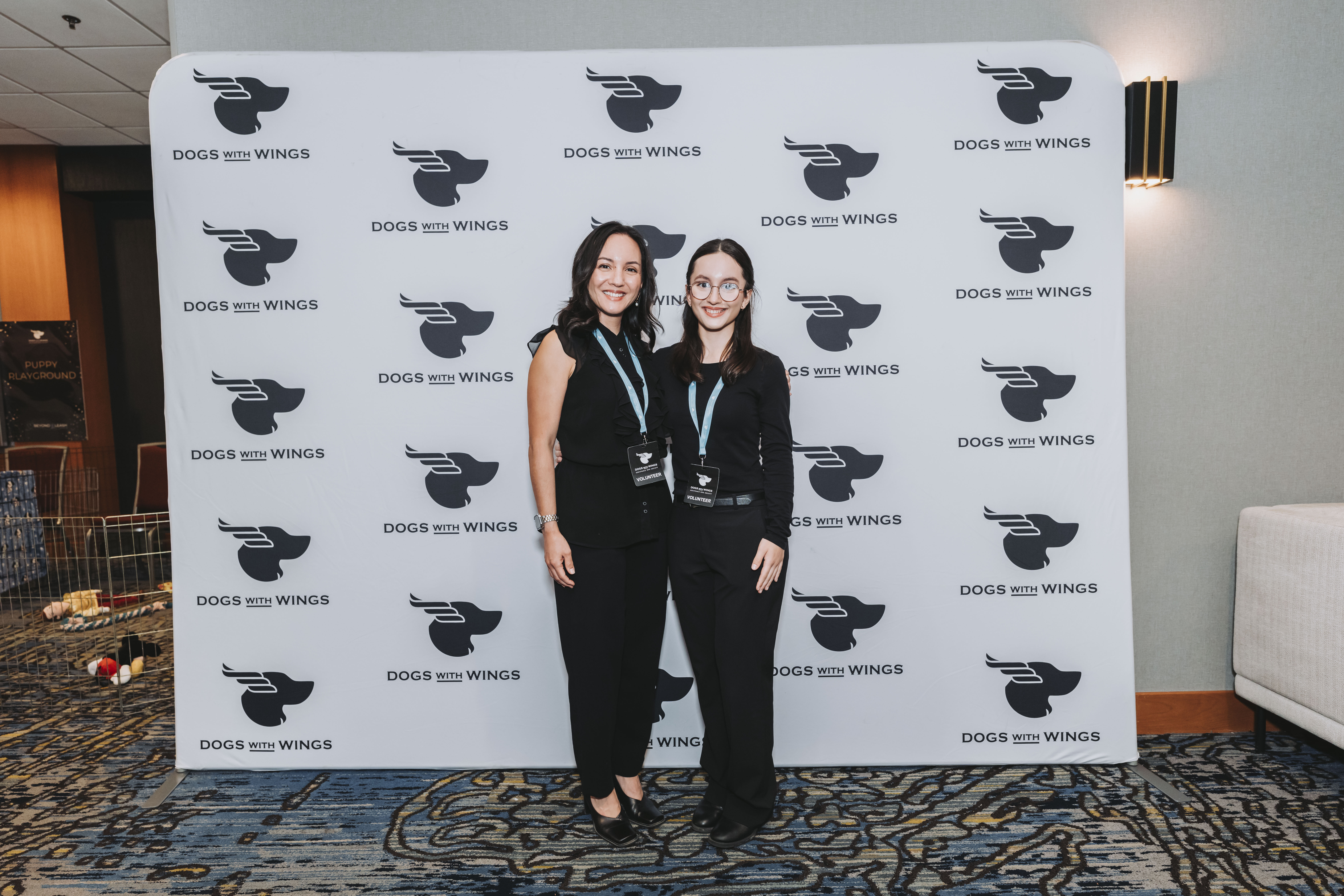 Two volunteers in lanyards smiling at the backdrop