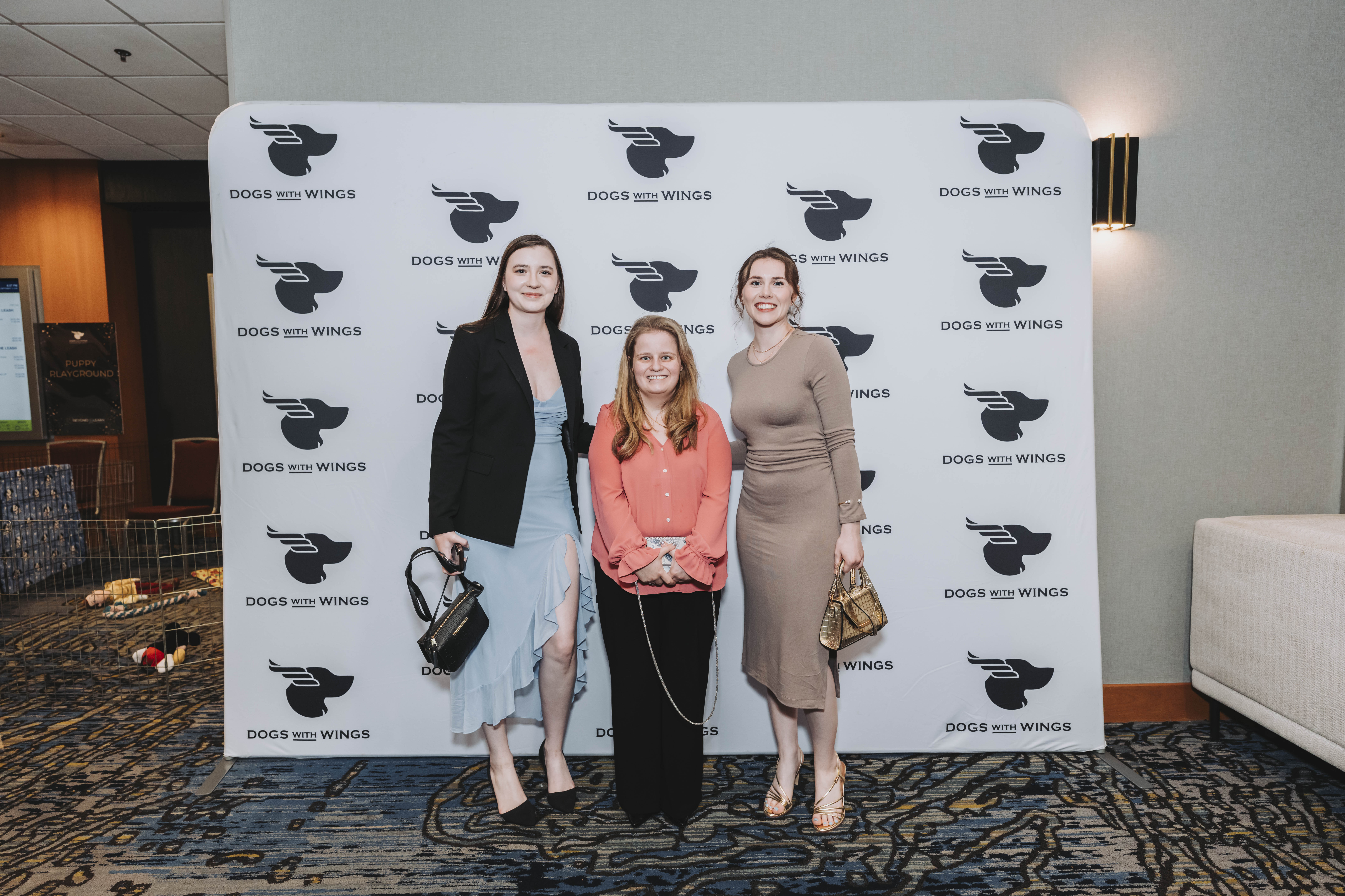 Three guests together in front of the Dogs With Wings backdrop
