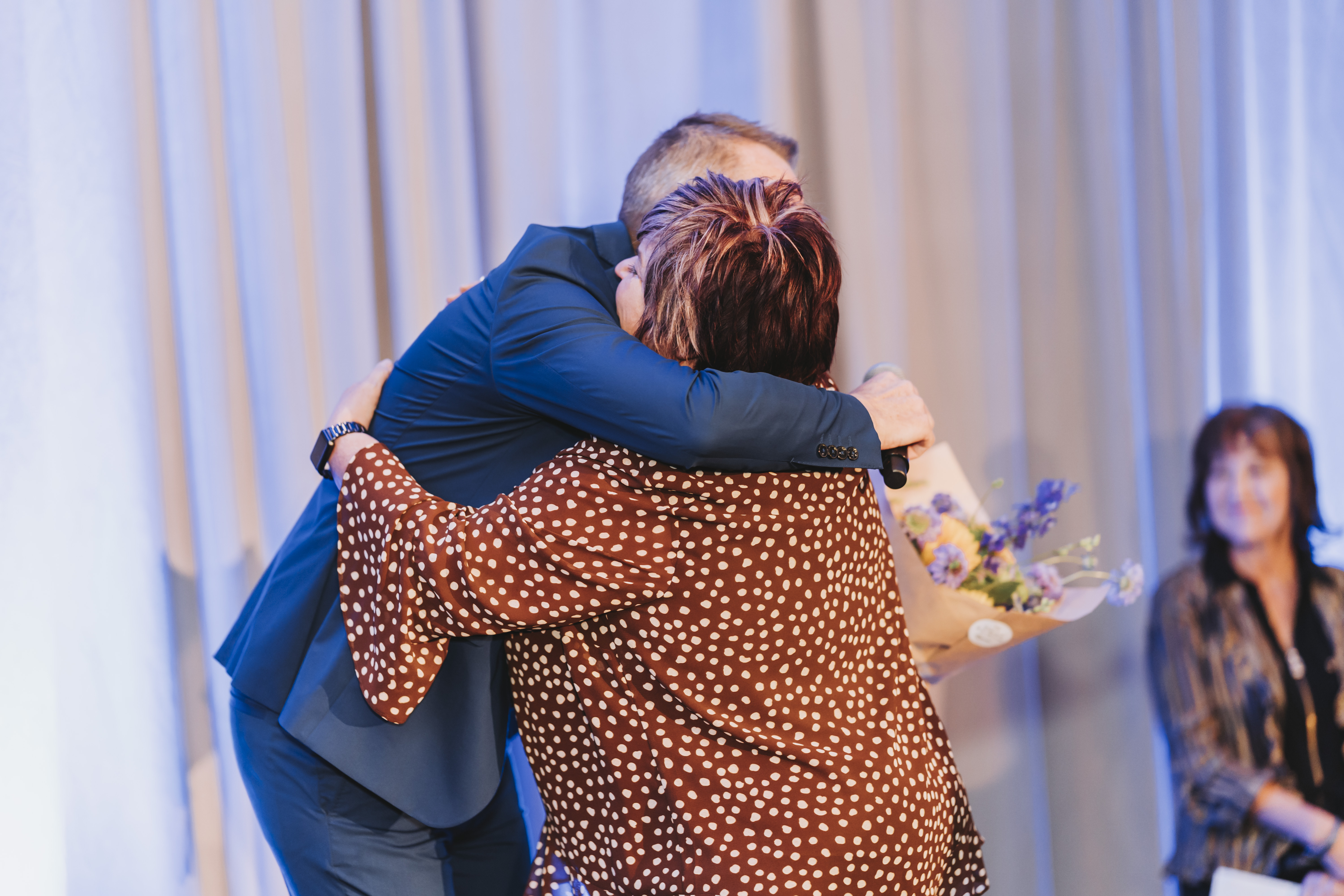 A heartfelt hug on stage as flowers are presented