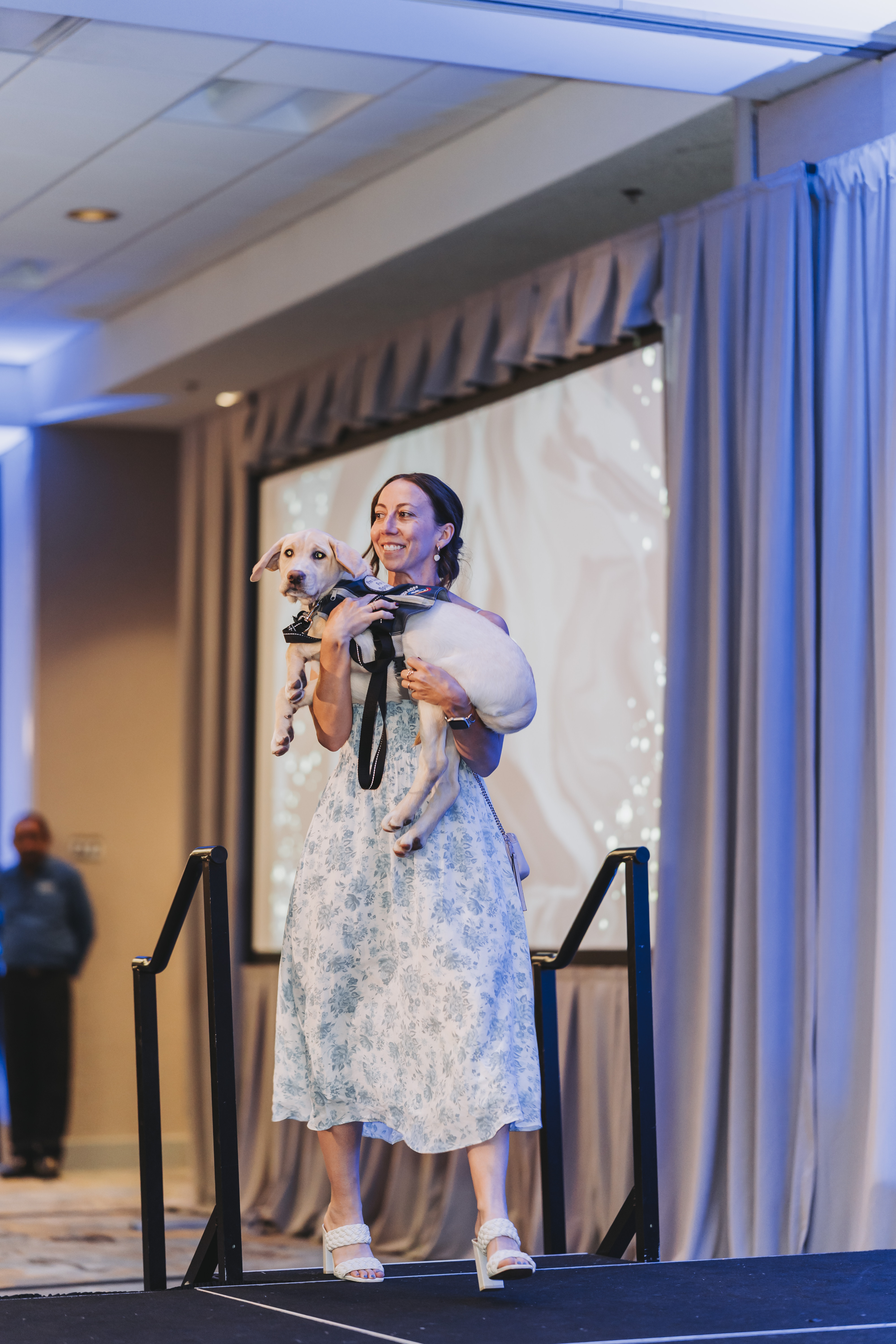 A guest carrying a cream puppy across the gala stage