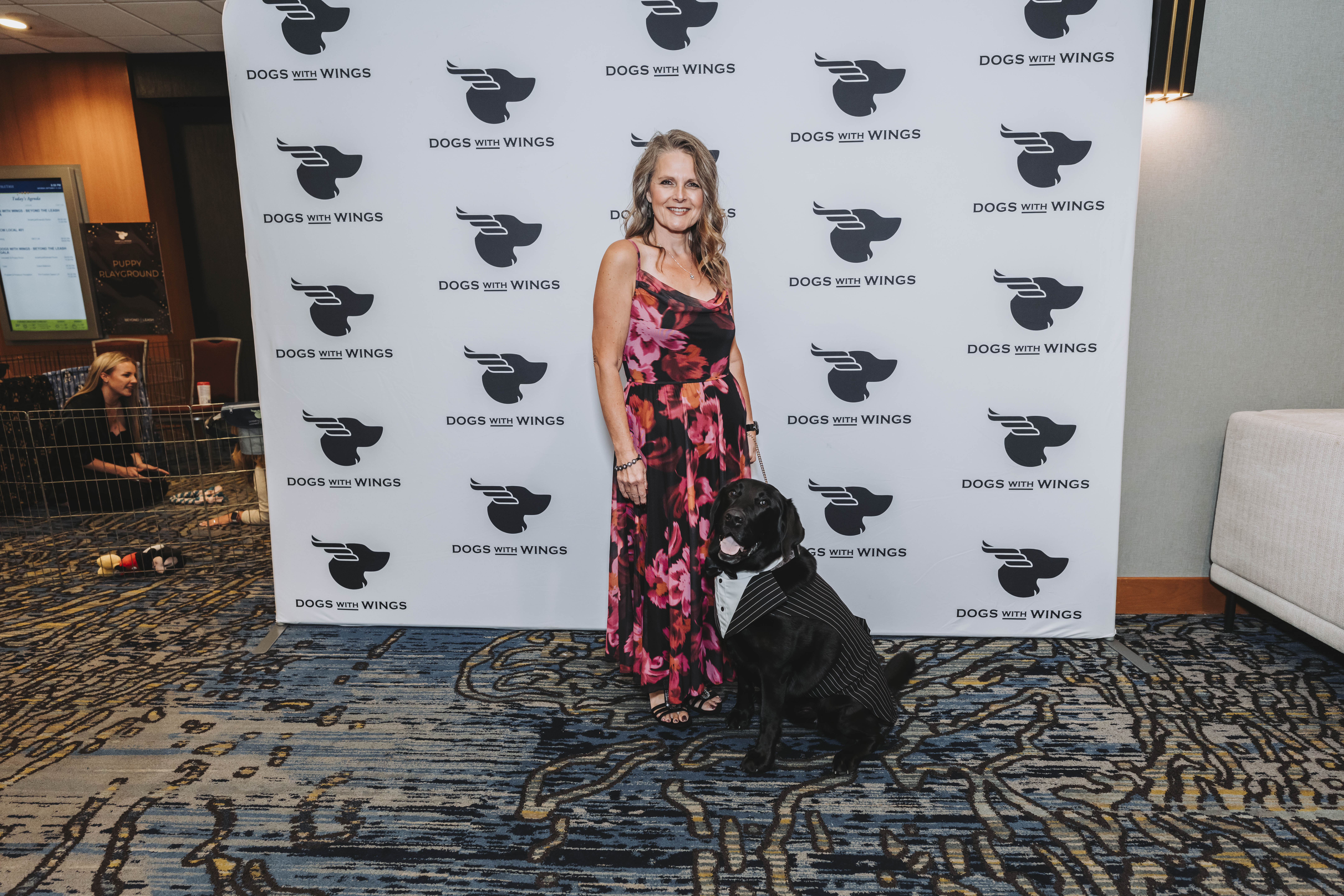 A guest in a floral maxi dress with a black dog in a tuxedo vest