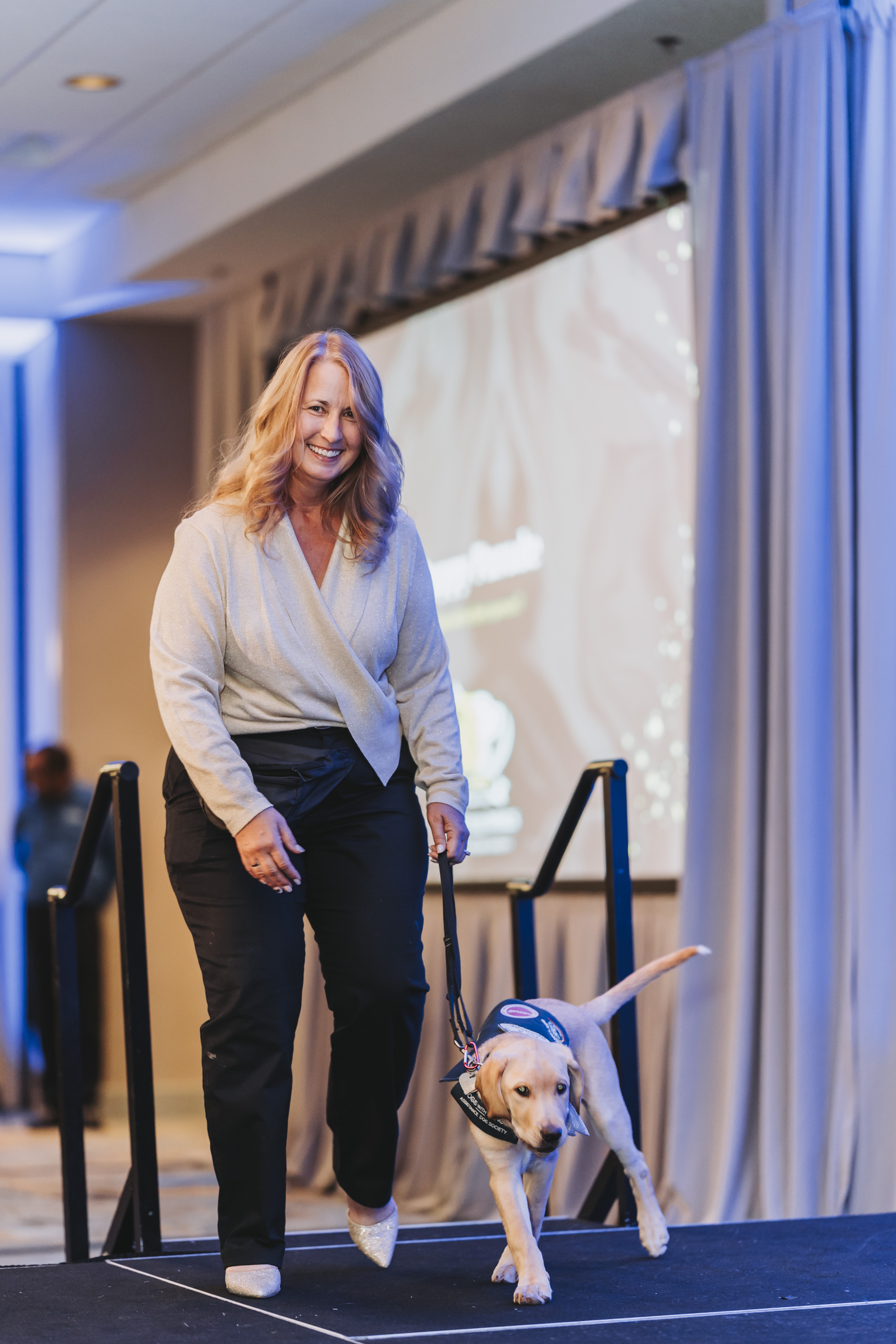 A guest walking a yellow Labrador puppy across the stage