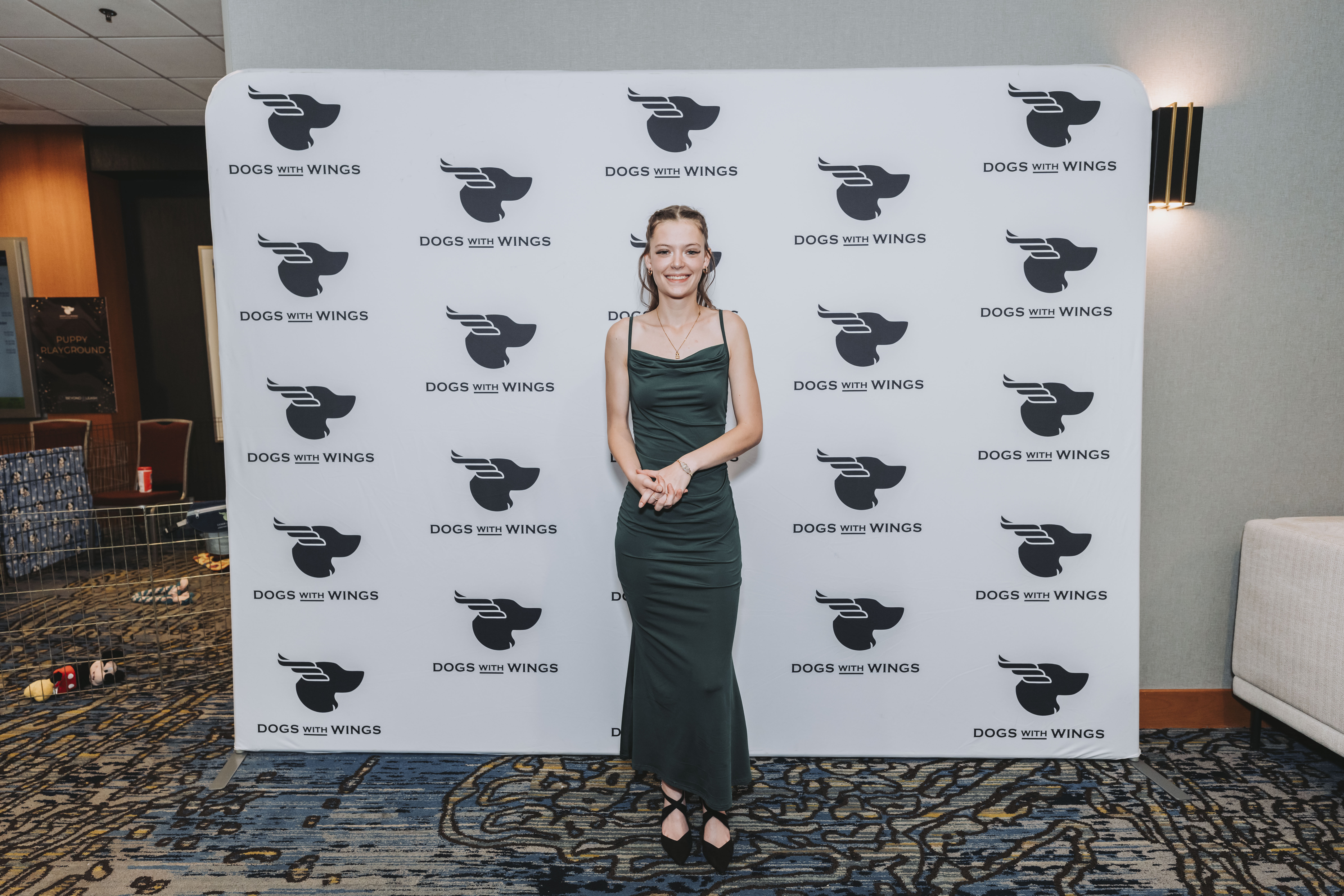 A guest in a dark green gown posing at the Dogs With Wings backdrop