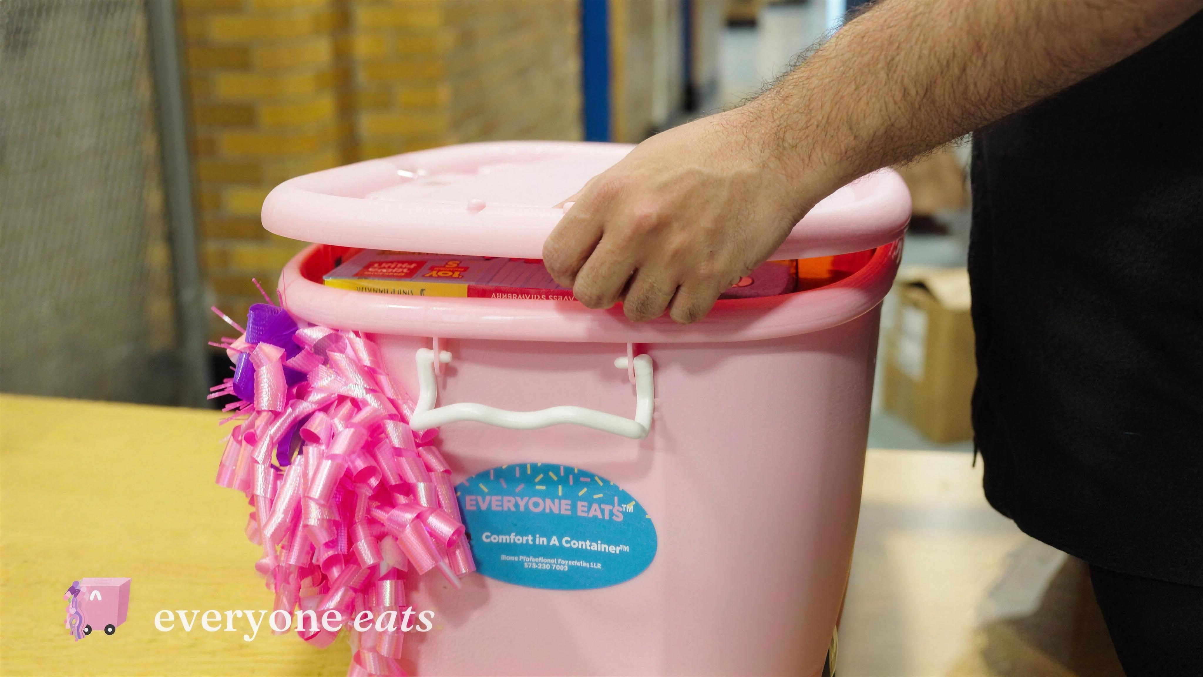 Close-up of the pink Comfort in a Container™ canister with the Everyone Eats™ label and a decorative bow.
