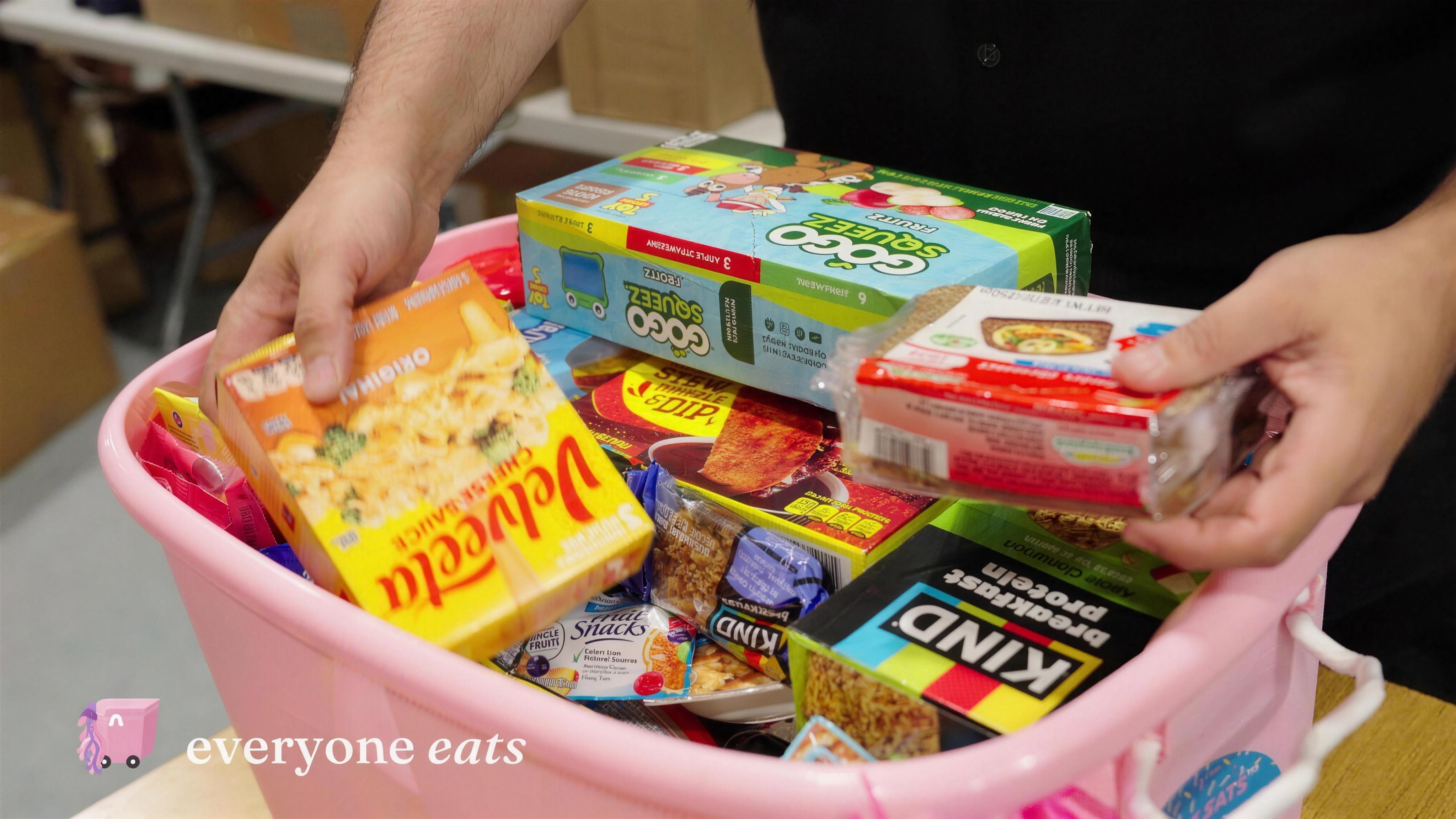 Hands filling the pink canister with shelf-stable meals and snack boxes.