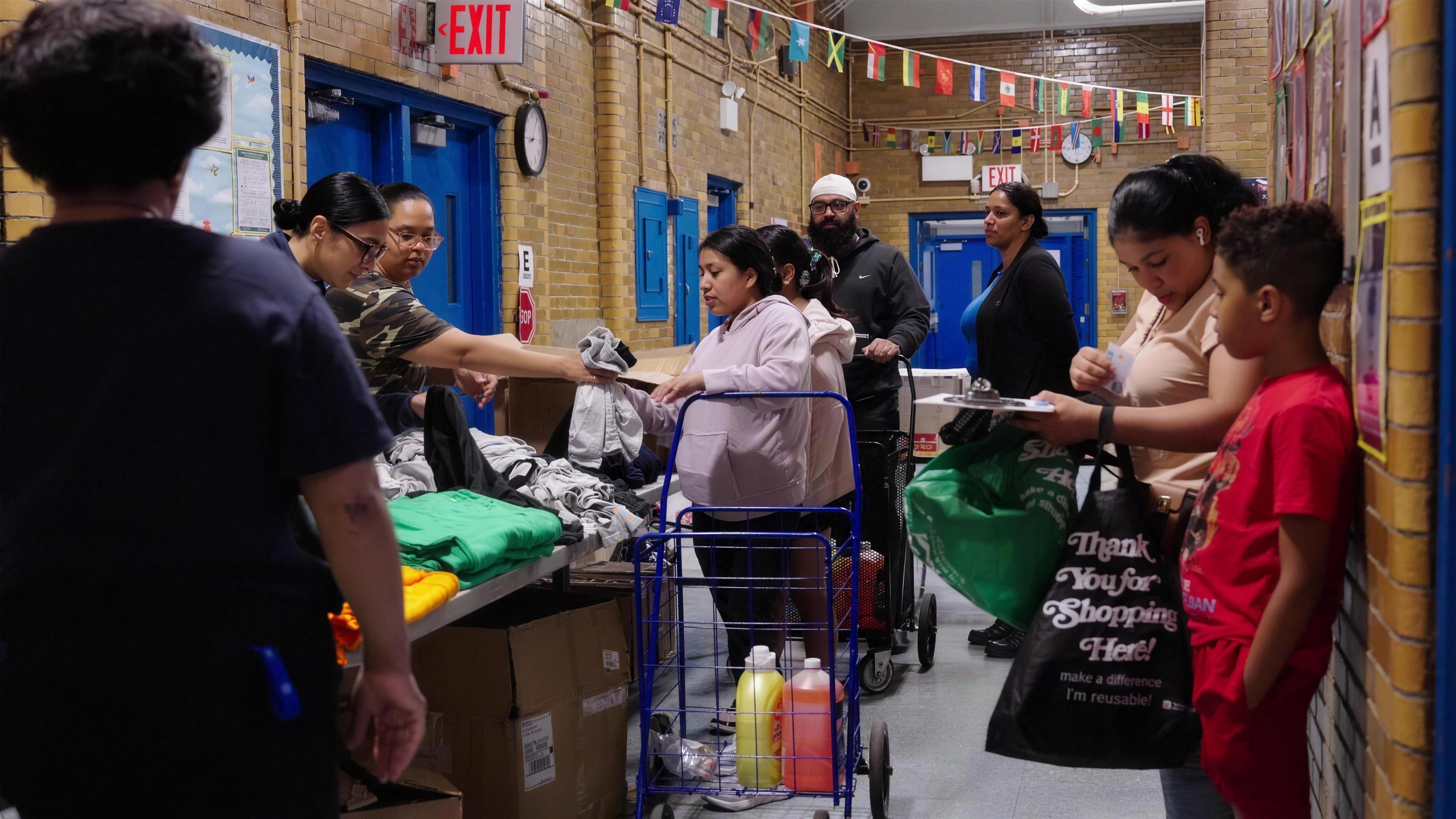 Volunteers handing folded clothing and groceries to a family at a school distribution day.