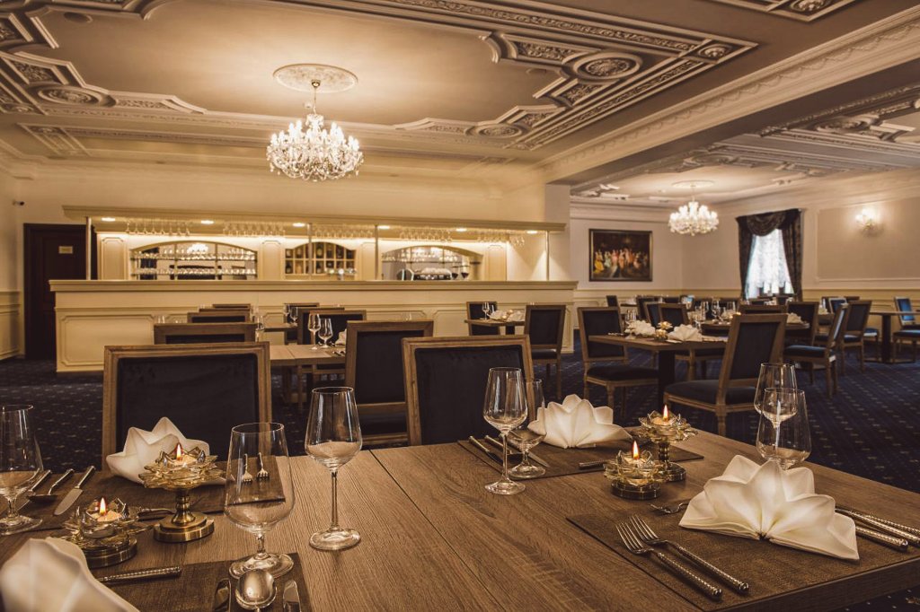 Elegantní restaurace se zlatými lustry, barem a slavnostně prostřenými stoly