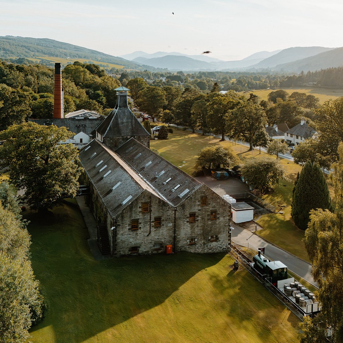 Aerial view of Aberfeldy Distillery and its warehouses at golden hour, with a cask train on the sidings