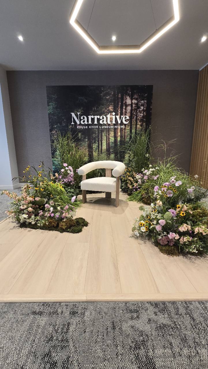 Front view of the Narrative photo setting with a forest backdrop, cream chair and surrounding flowers.