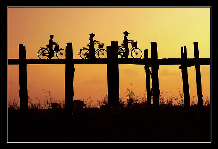 Silhouette of cyclists crossing a wooden bridge at sunset, Mandalay, Myanmar