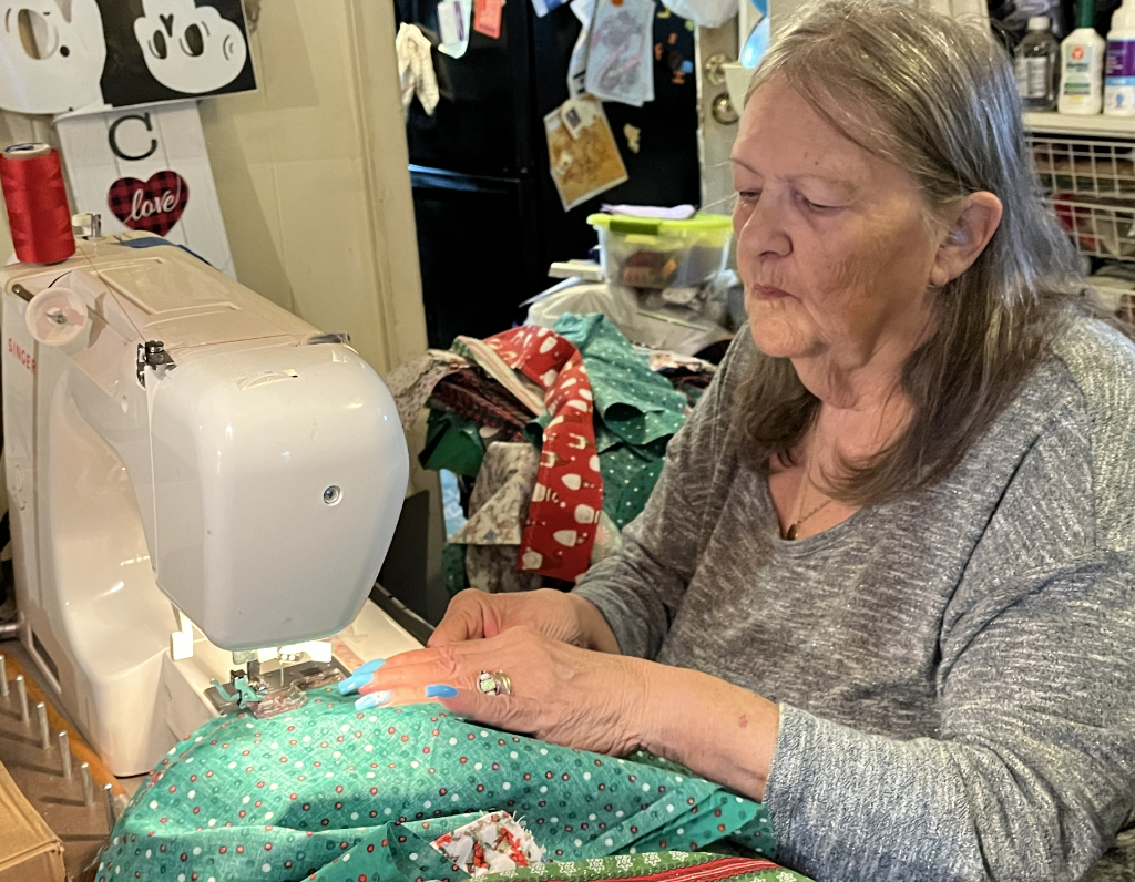 Woman with grey hair sewing a Christmas stocking at her machine