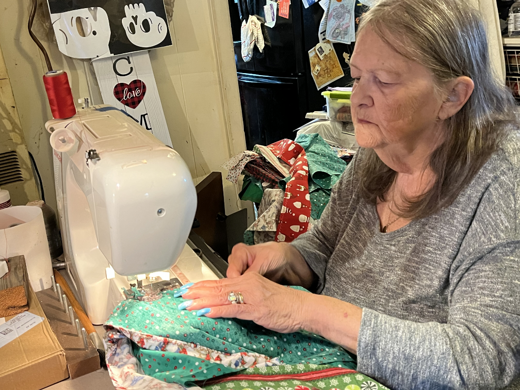 Woman in grey sweater sewing festive fabric on a Singer machine