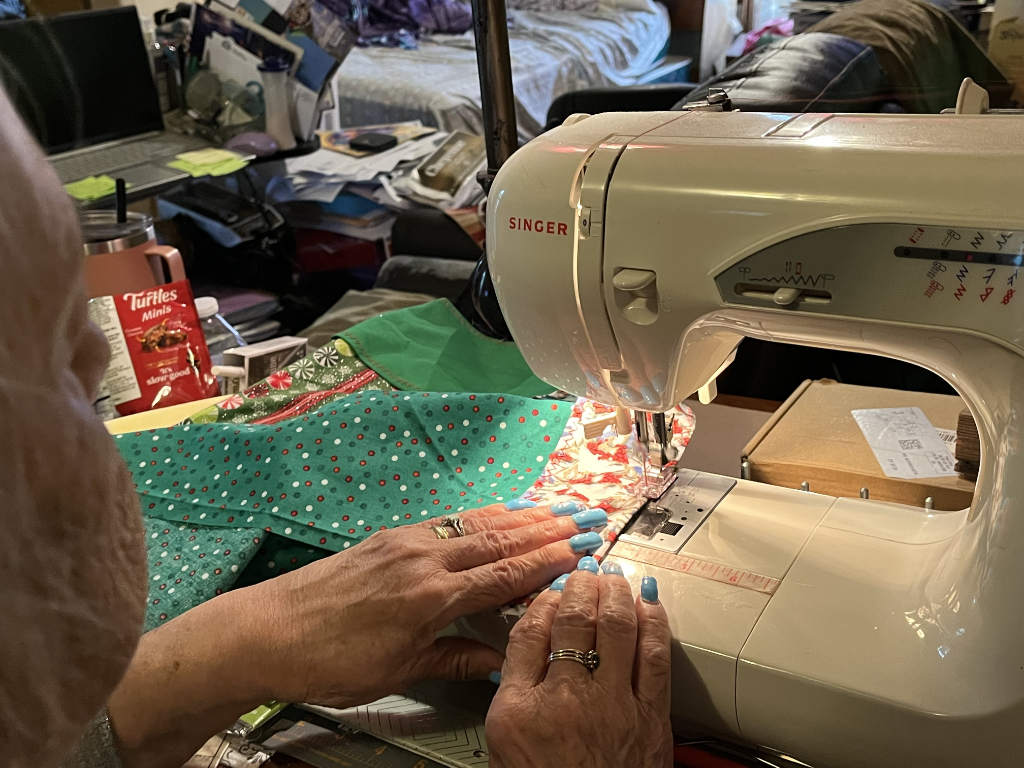 Hands guiding holiday fabric through a Singer sewing machine