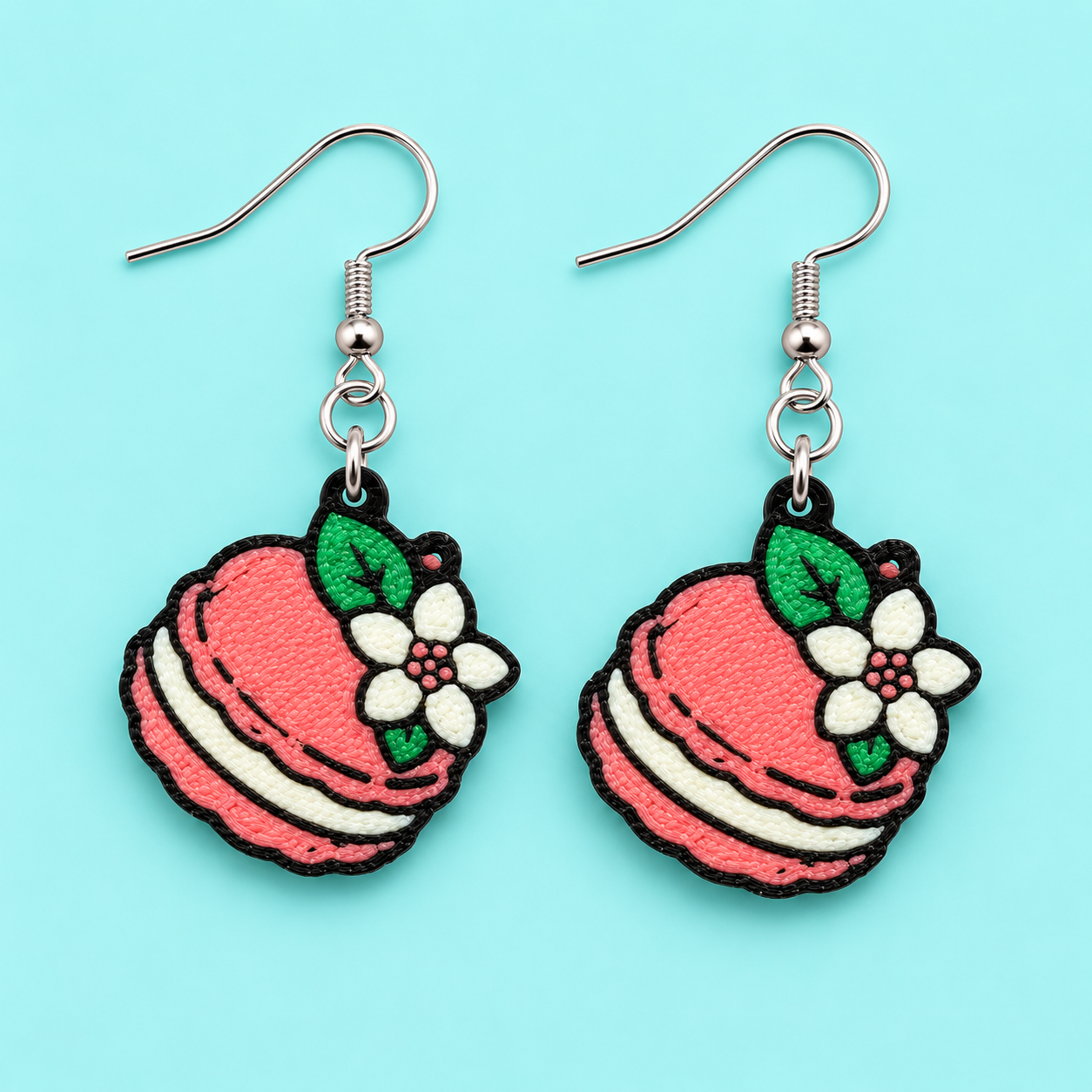 Pink macaron earrings with white flowers and green leaves on a light aqua blue background