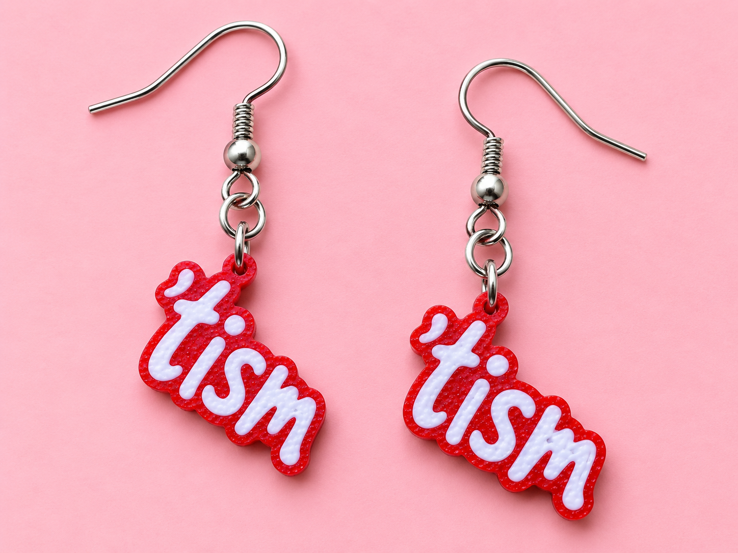 Red earrings spelling the word tism in raised white bubble letters