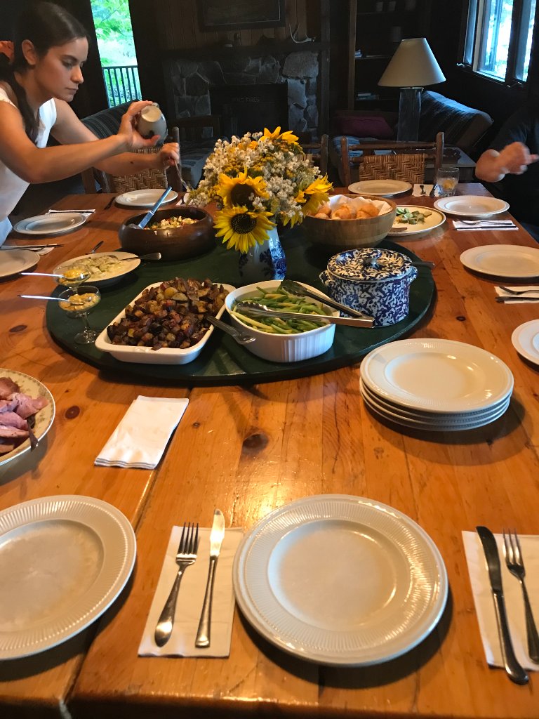 Long pine dining table set family-style with fresh food and sunflowers at Gunn Lake Lodge