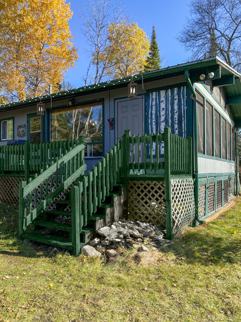 The green main cottage with its deck and stairs framed by autumn trees