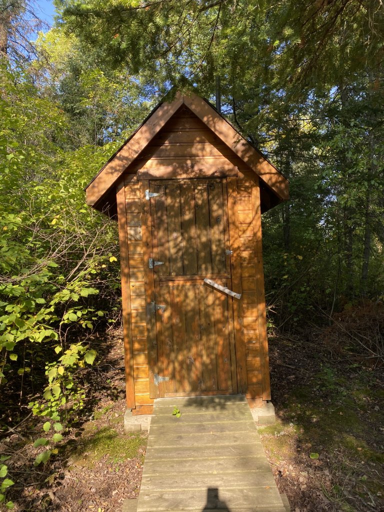 A cedar outhouse tucked into the forest along a wooden path